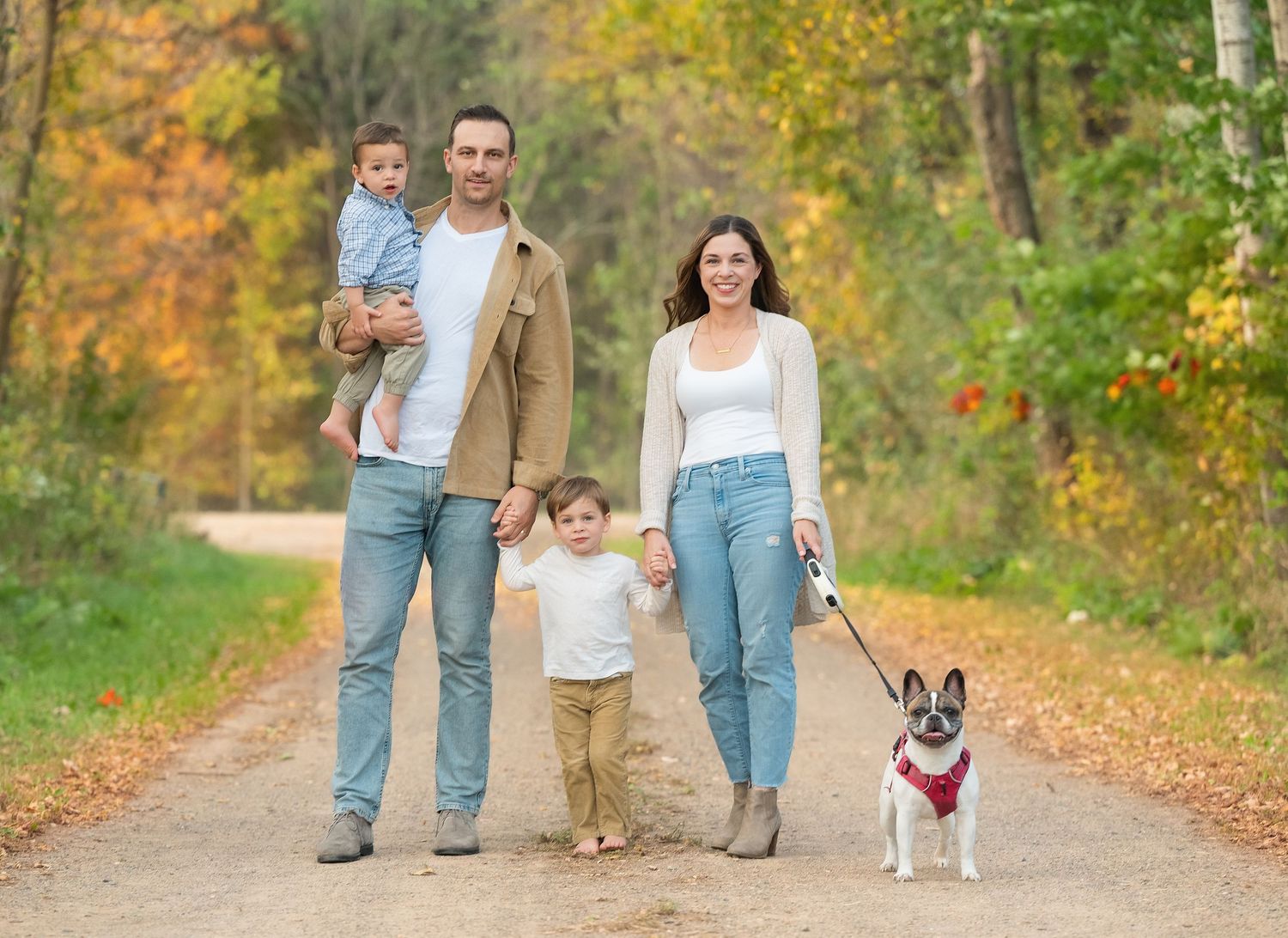 In central Minnesota a Family walking on autumn path with their Boston Terrier dog among colorful fall foliage.