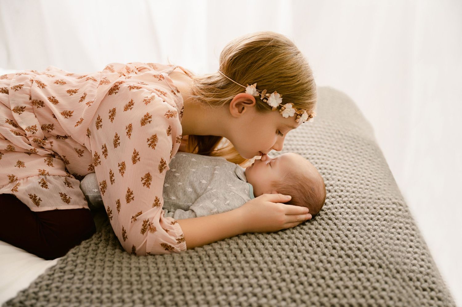 A tender moment captured between mother and baby lying on a gray knit blanket.