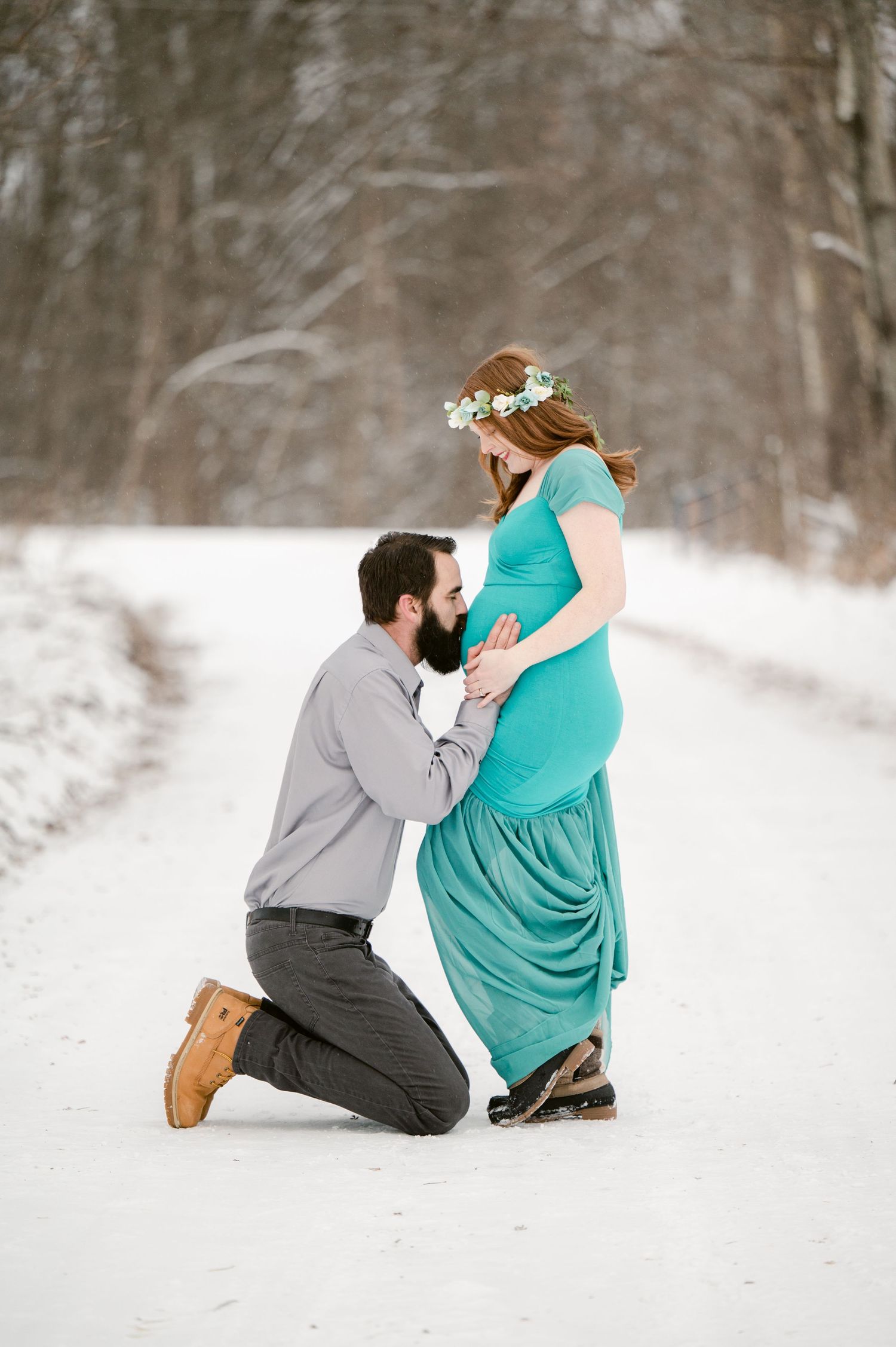 The Clark’s romantic winter maternity photoshoot series in a winter scene shows a couple in a tender moment on snow covered ground.