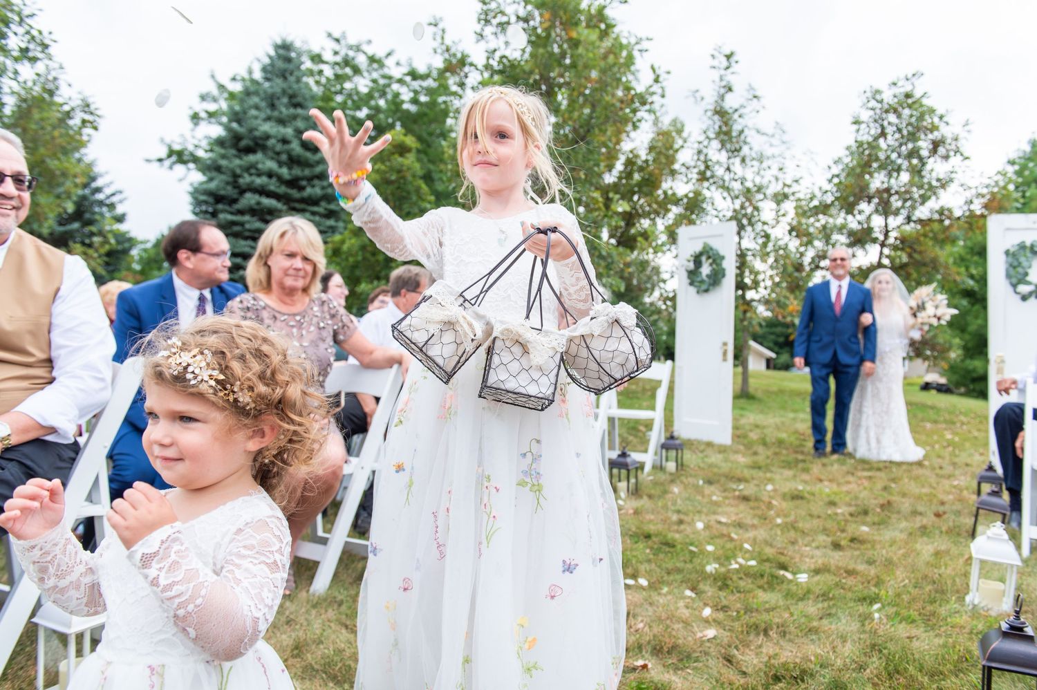 Wedding guests enjoy outdoor ceremony with white chairs on grassy hillside.
