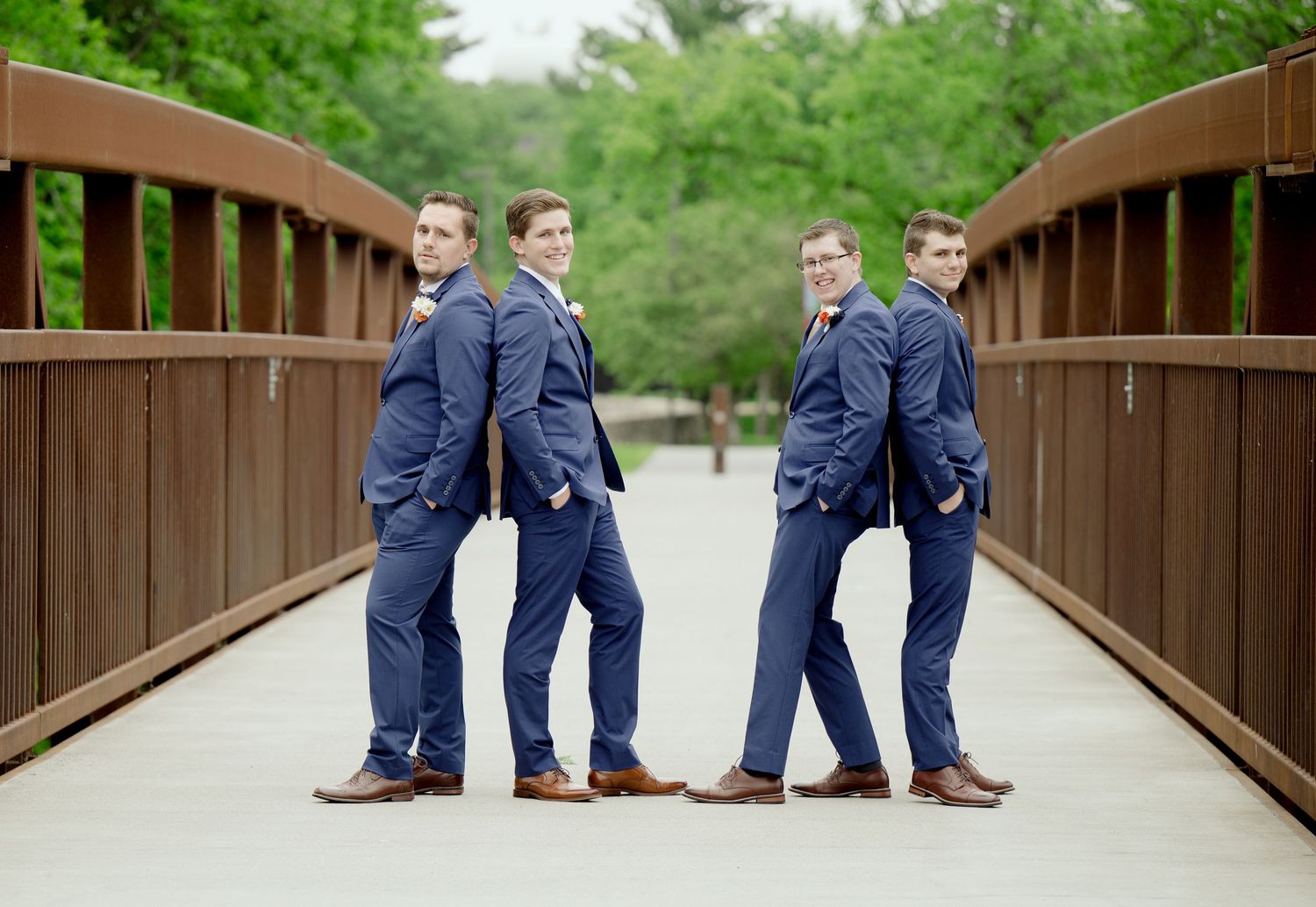 Groomsmen in navy suits posing playfully on a wooden bridge for wedding photos.
