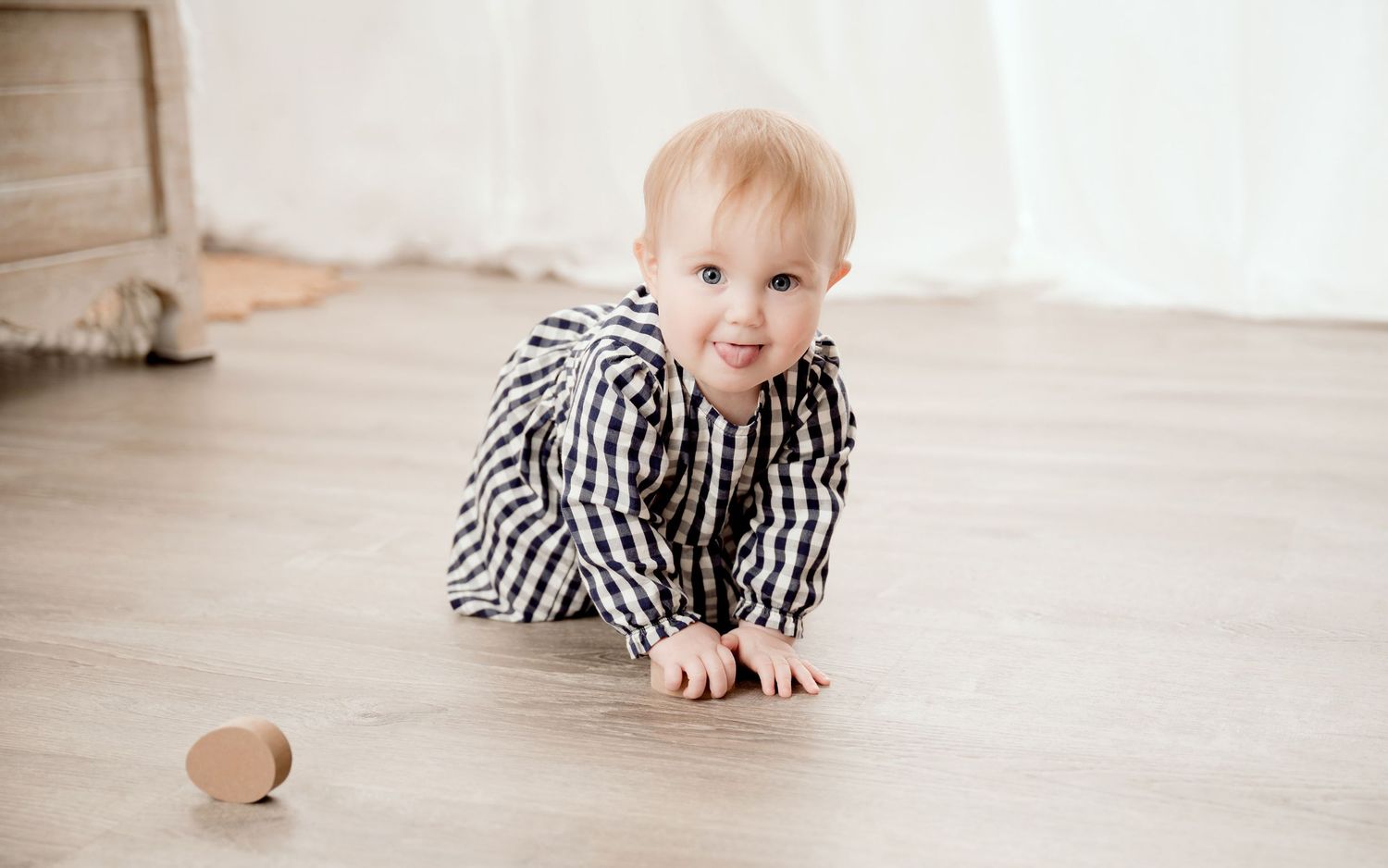 Baby in black and white checkered outfit crawling on hardwood floor.