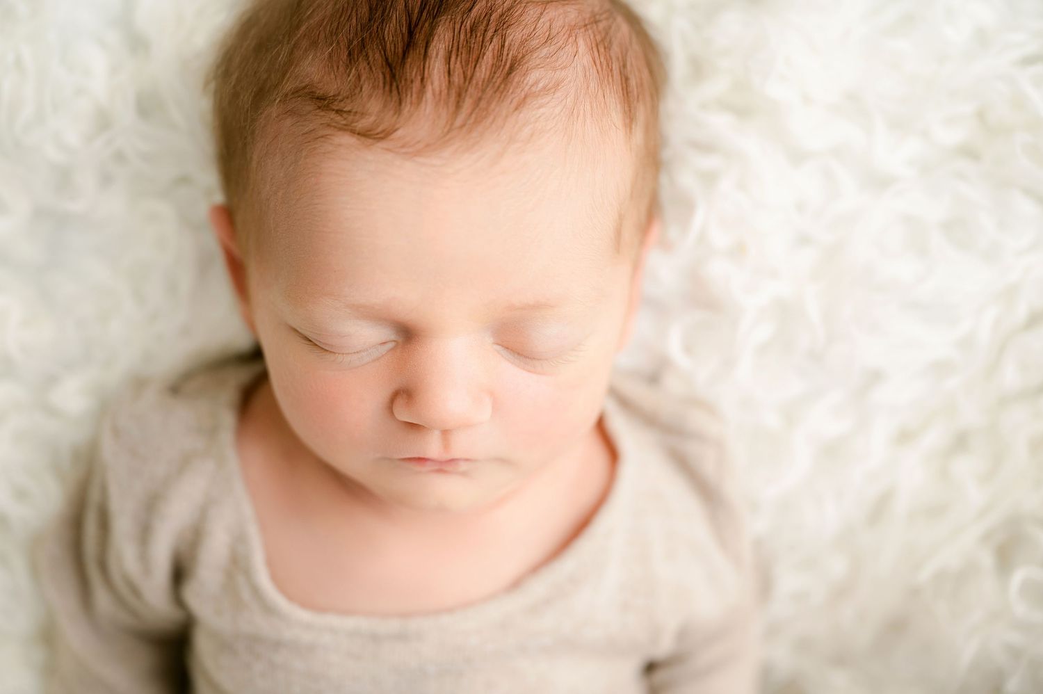 Central MN Baby Photos - Peaceful newborn baby sleeping on a soft white fluffy blanket wearing a light gray onesie.