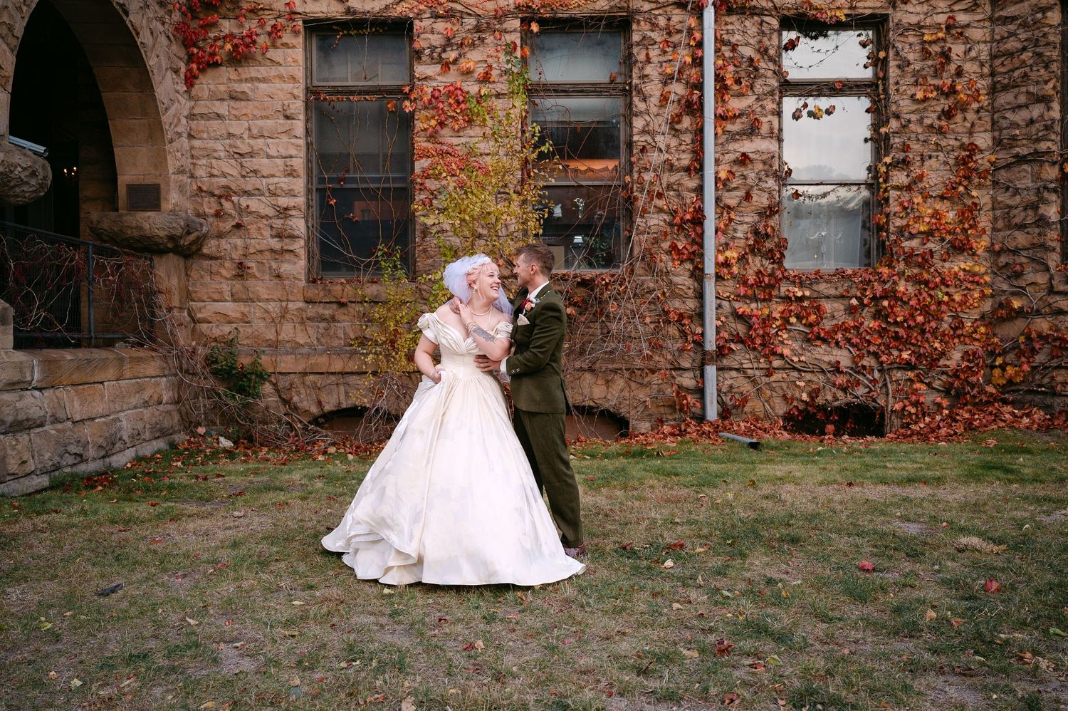 Central MN Wedding Photos | Bride and groom share romantic kiss outside historic stone building in autumn.