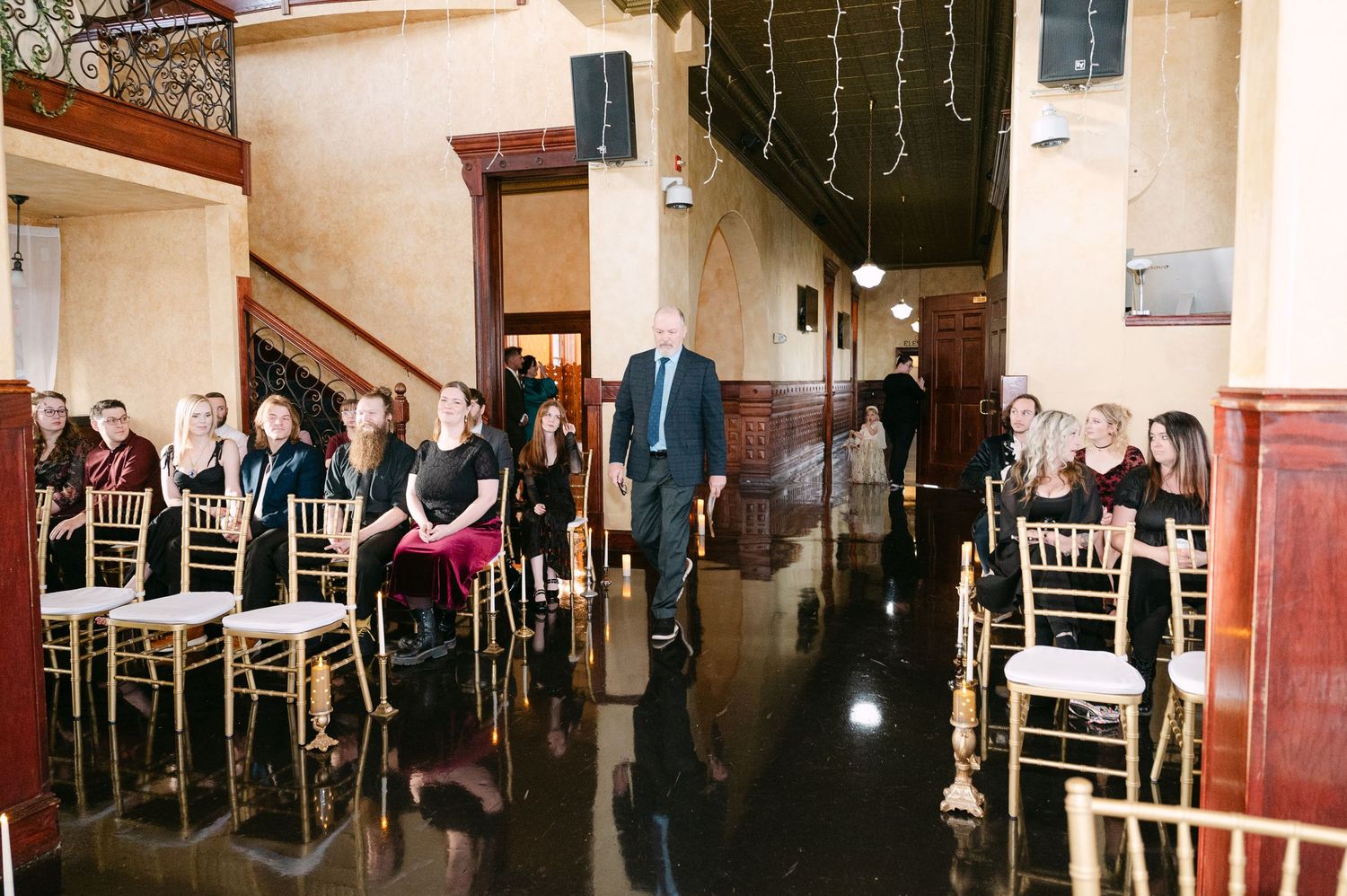 Central MN Wedding Photos | Wedding guests seated in gold chiavari chairs awaiting ceremony in an elegant venue with black floors.