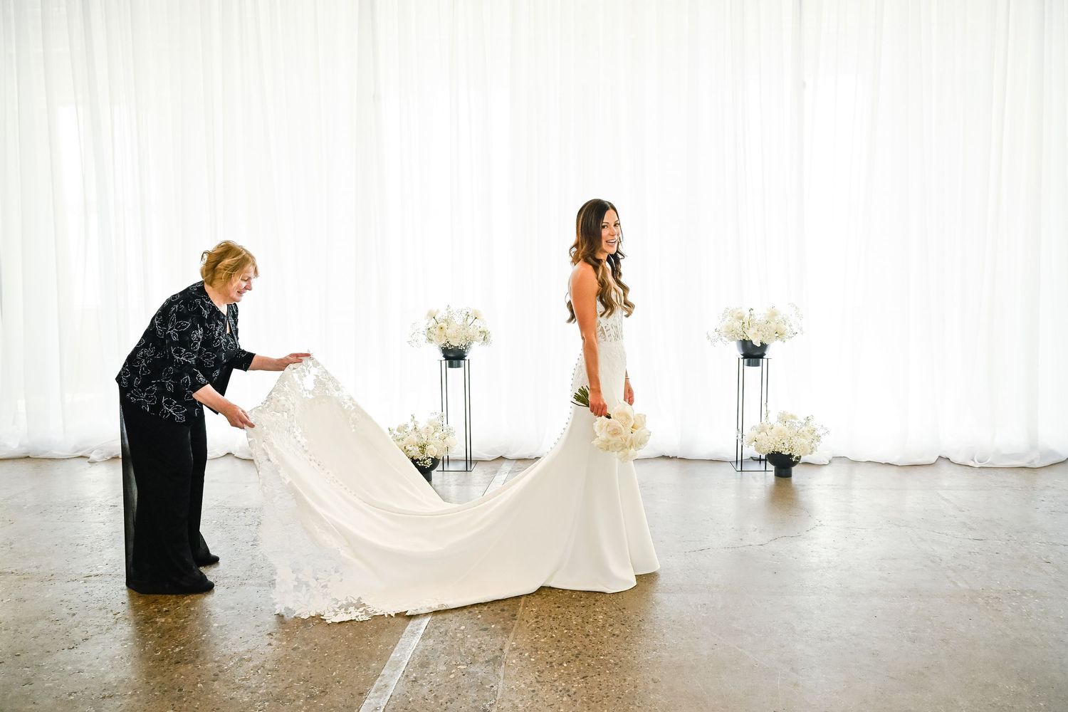 Wedding dress being arranged for photos in a bright white room.