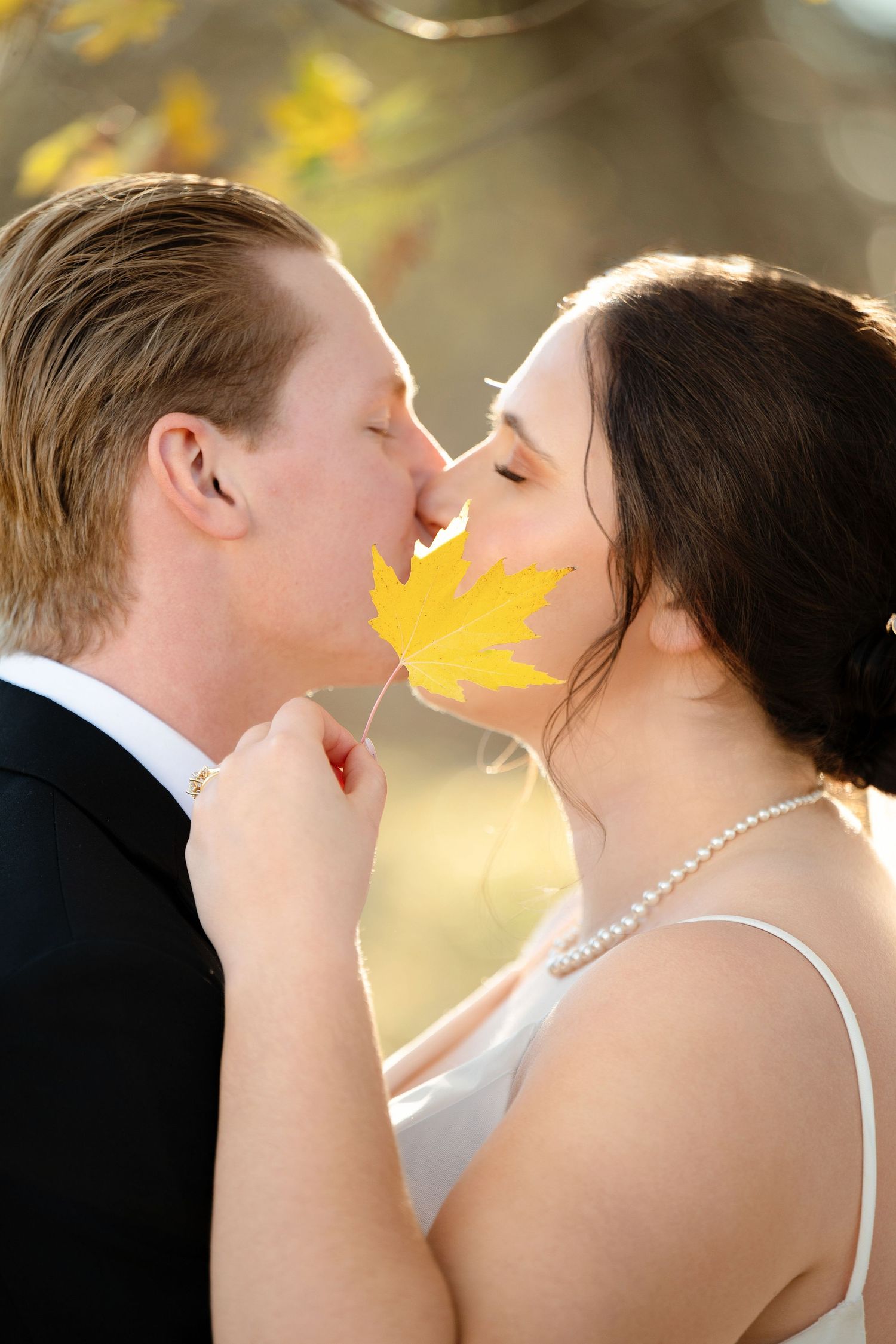 A romantic wedding couple shares an intimate moment in golden sunlight with autumn leaves in the background.