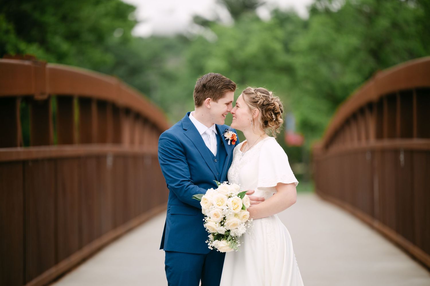 Elegant couple sharing romantic moment on wooden bridge during wedding photoshoot.
