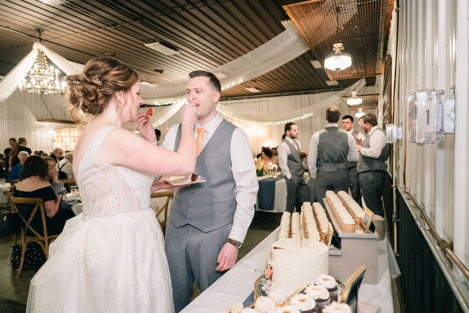 Bride feeding groom cake at wedding dessert table reception.