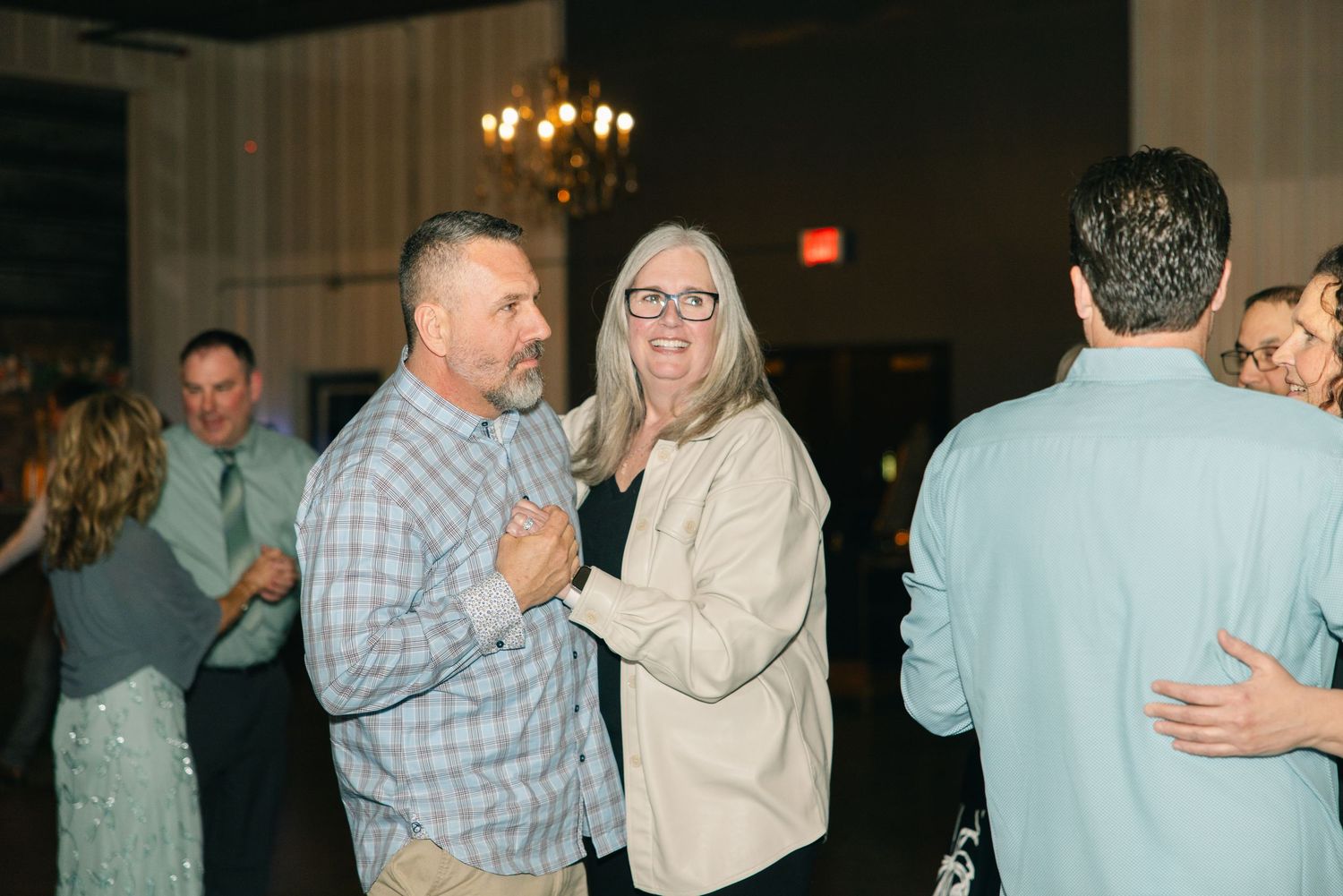 Wedding guests smile and dance together on the reception dance floor during the celebration.