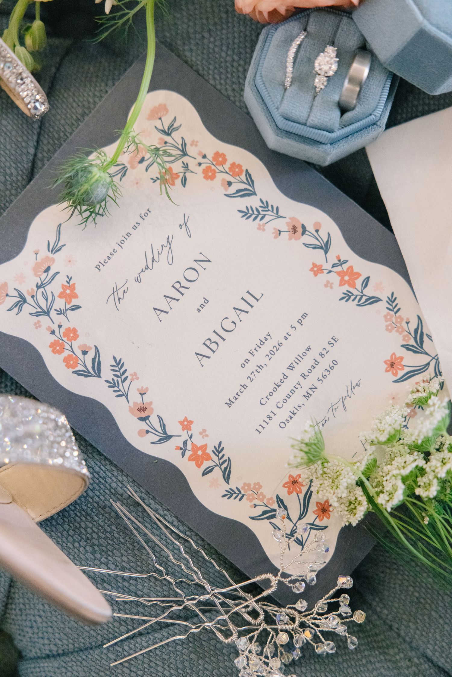Wedding invitation for Aaron and Abigail with floral design, engagement ring, and wedding bands on blue velvet.