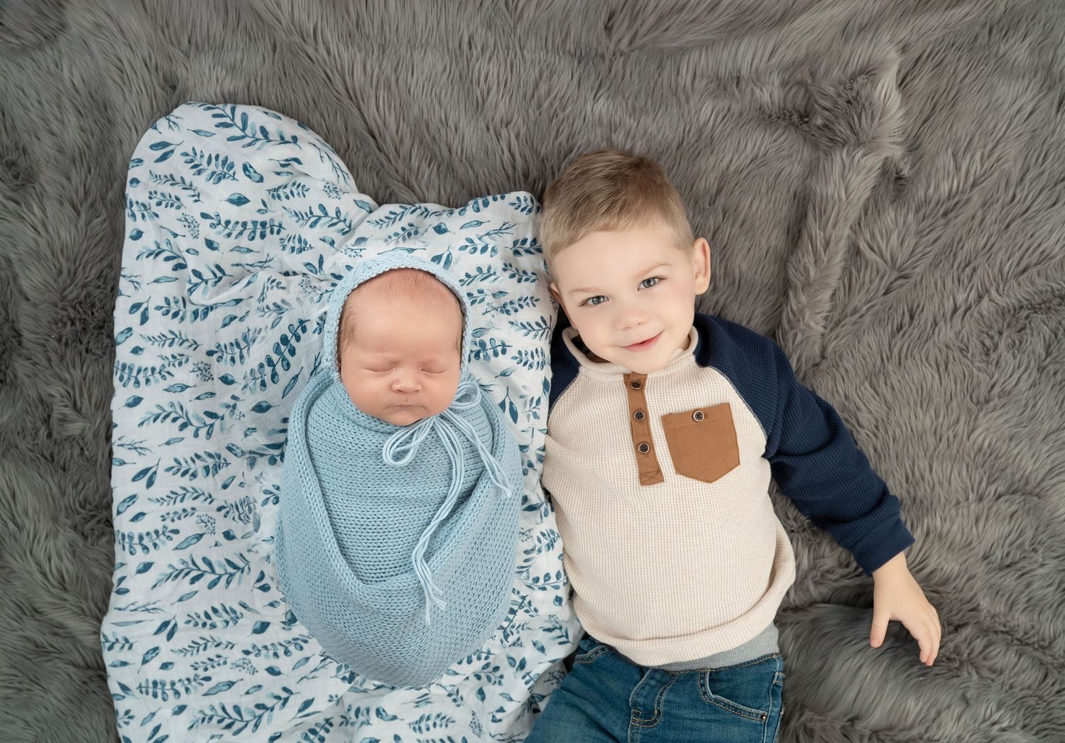 In central Minnesota a series of overhead shots showing a baby lying on soft gray bedding wearing blue and cream colored outfits.