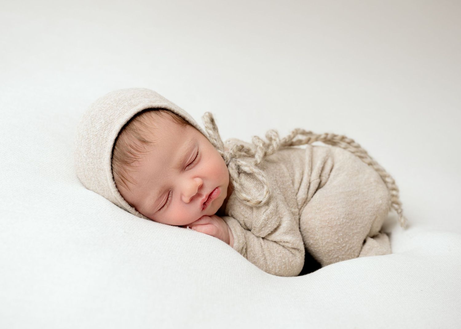 Minnesota Best newborn photographer -Baby sleeping peacefully in soft beige attire while curled up in natural light against white backdrop.