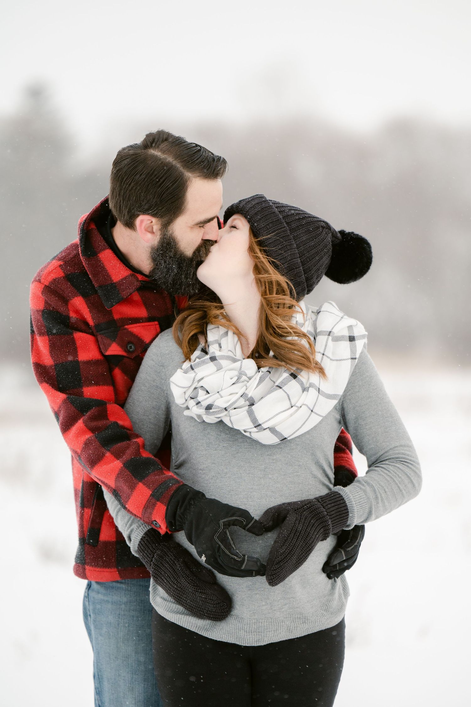 The Clark’s romantic winter maternity photoshoot series in Foreston mn embracing in red plaid and grey outfits against a snowy backdrop.