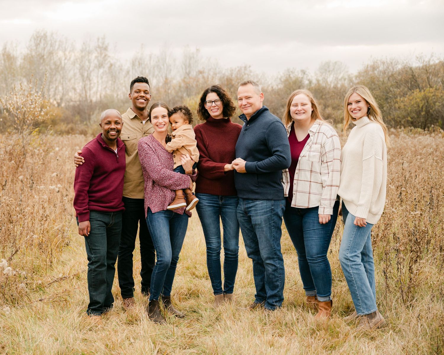 A group of people posing together in a field of tall grass during an autumn photoshoot at golden hour.