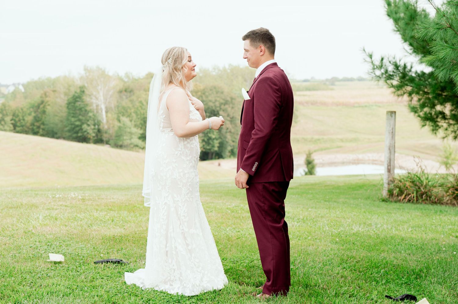A couple shares their first look moment in a lush outdoor wedding setting with rolling hills in the background.