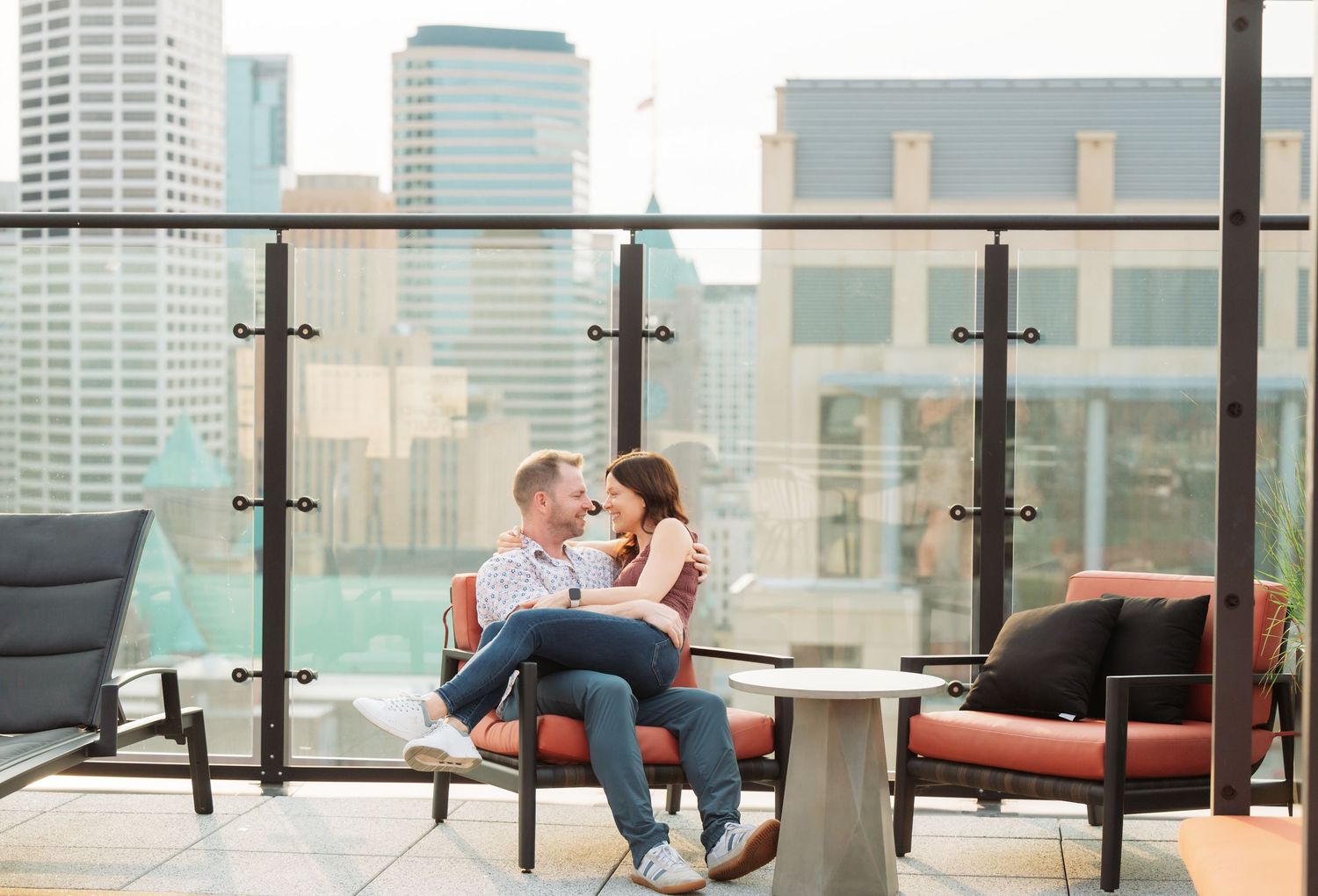 Modern rooftop lounge area with red cushioned seating and glass walls overlooking a city skyline.