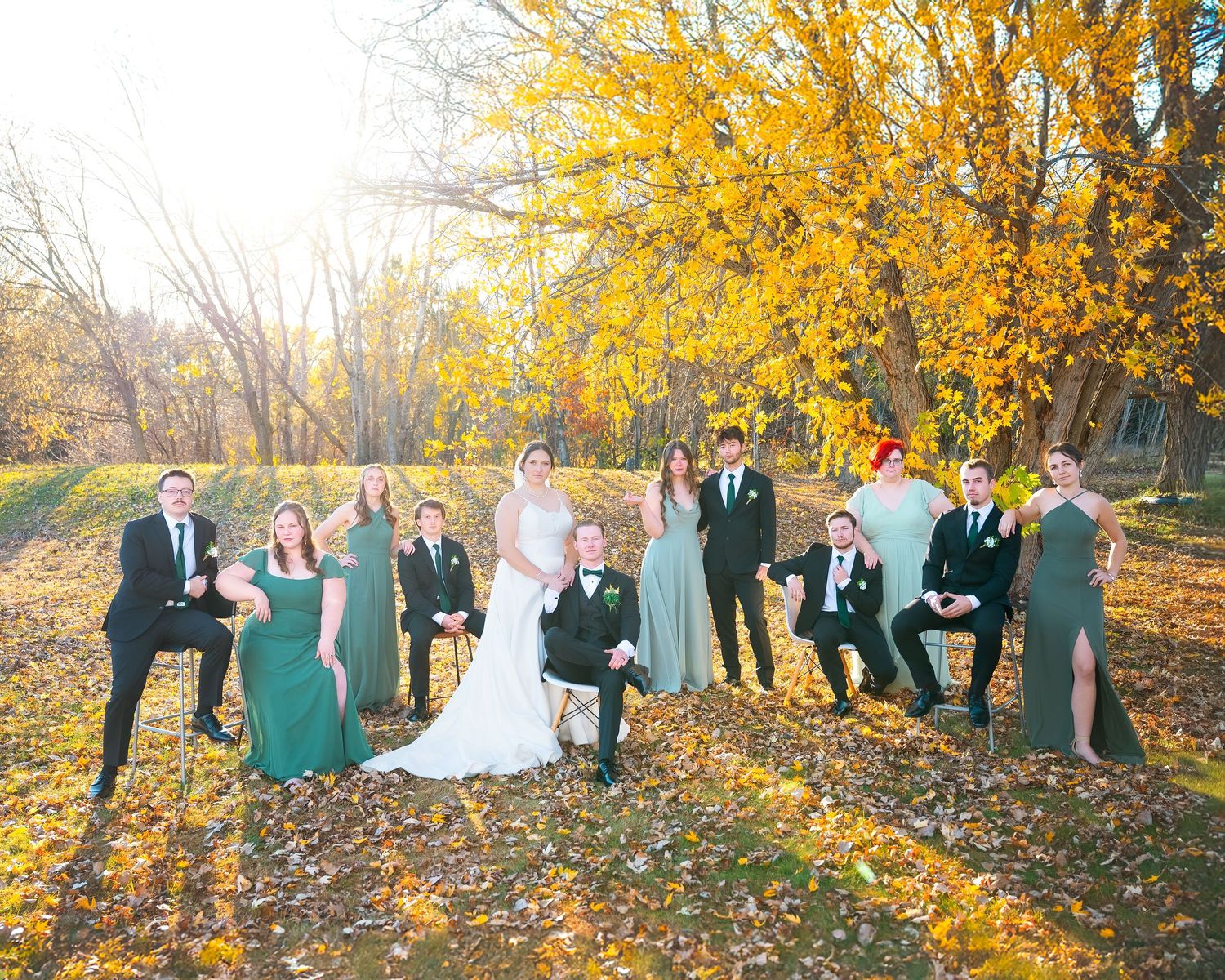 A wedding party poses together under vibrant yellow autumn trees during golden hour.