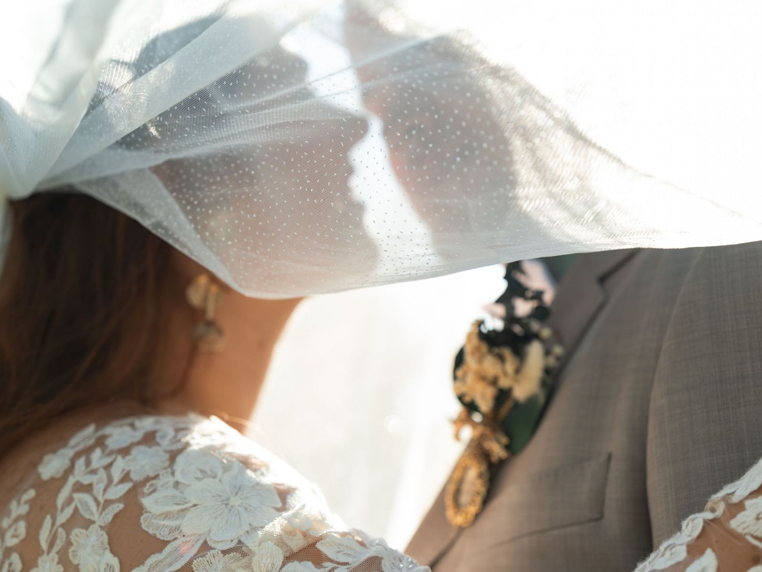 White lace wedding veil detail with delicate floral patterns and soft light shining through the sheer fabric.