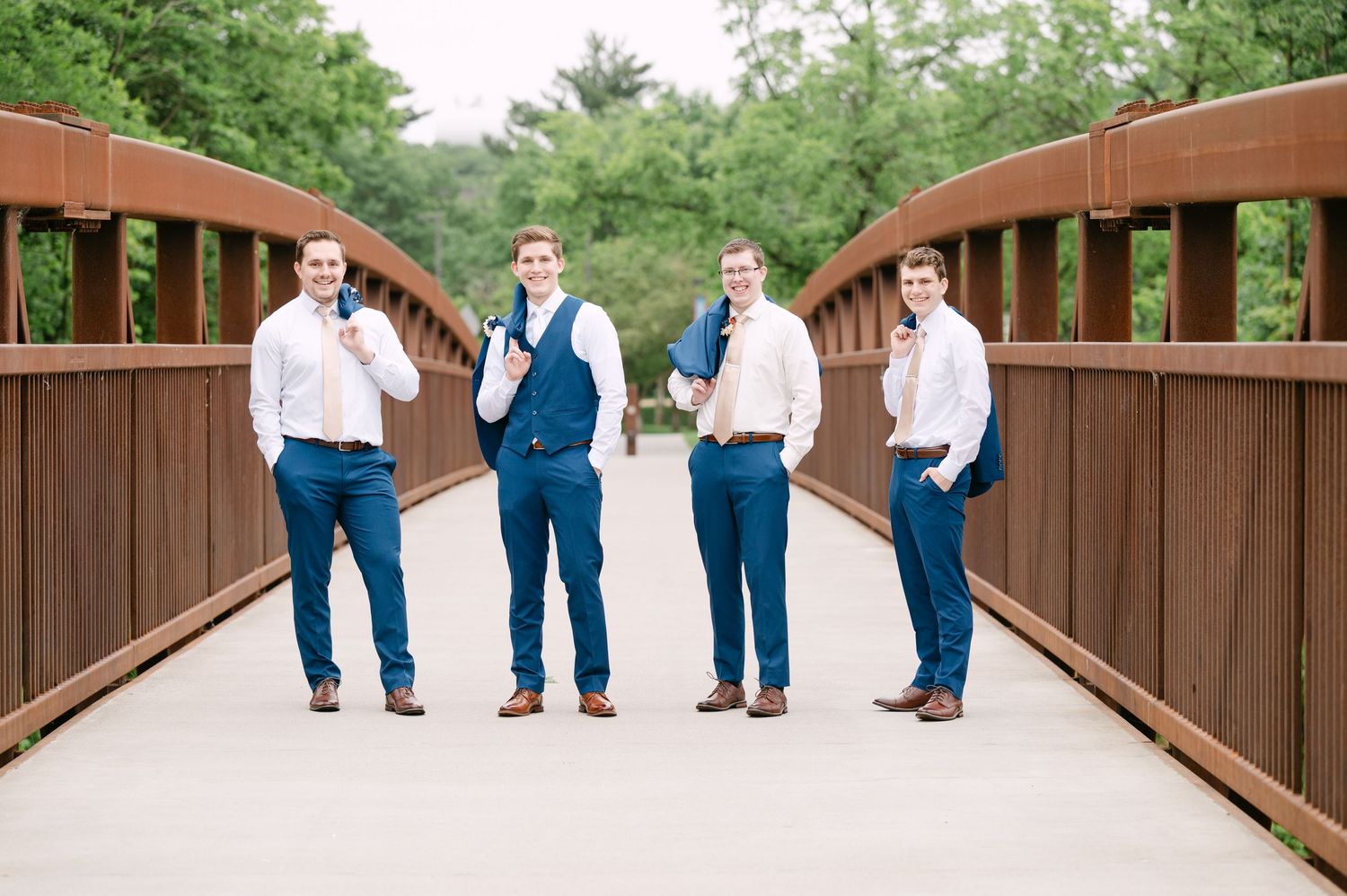 Wedding party members in blue and white attire walking across a wooden bridge.