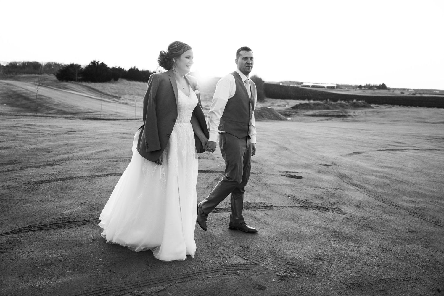 Black and white photo of a bride and groom walking hand in hand across a sandy landscape.