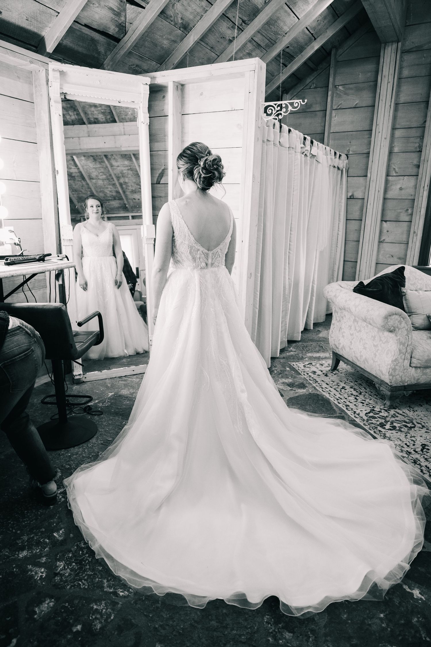 Black and white photo of bride in elegant gown with train viewing reflection in mirror.