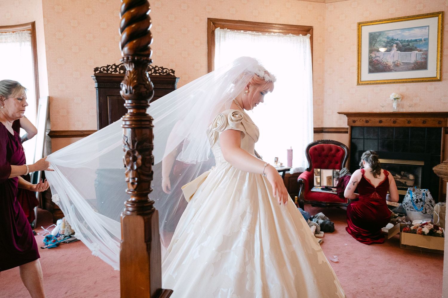 Central MN Wedding Photos | Bride in vintage-style ballgown and veil being assisted by bridesmaids in purple room.