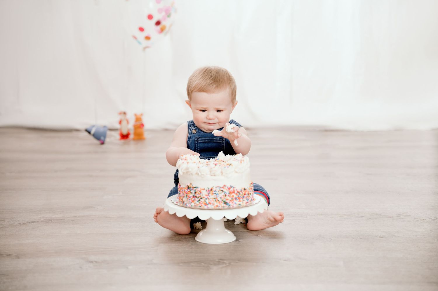Central MN cake smash Photography - Baby sitting on floor smashing a white sprinkle birthday cake during first birthday cake smash photo.