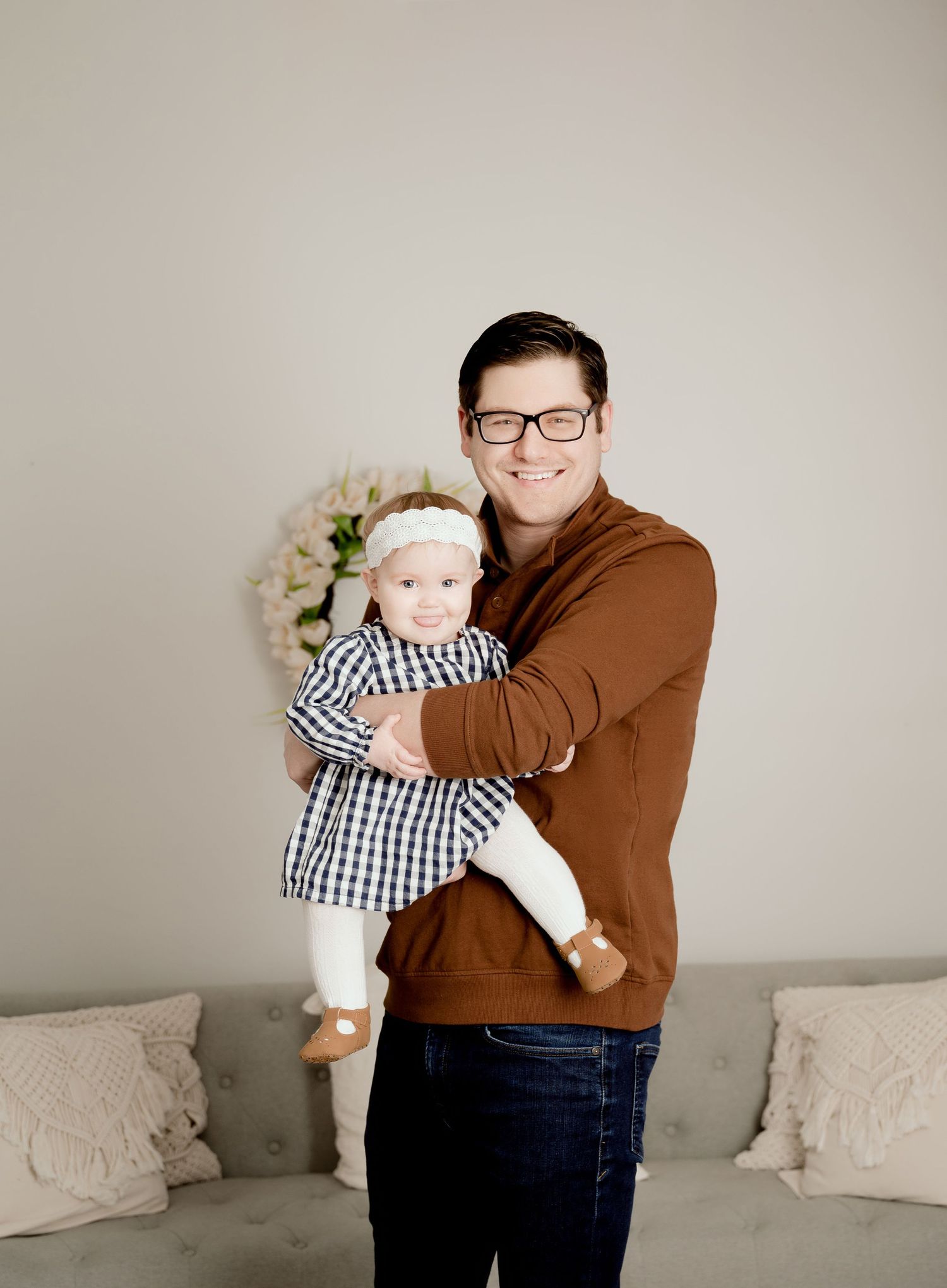 Parent holds smiling baby in checkered outfit against neutral studio background.