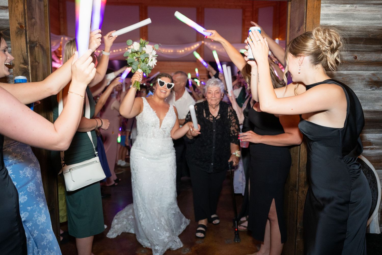 Bride exits reception through tunnel of glowing light sticks held by cheering wedding guests.