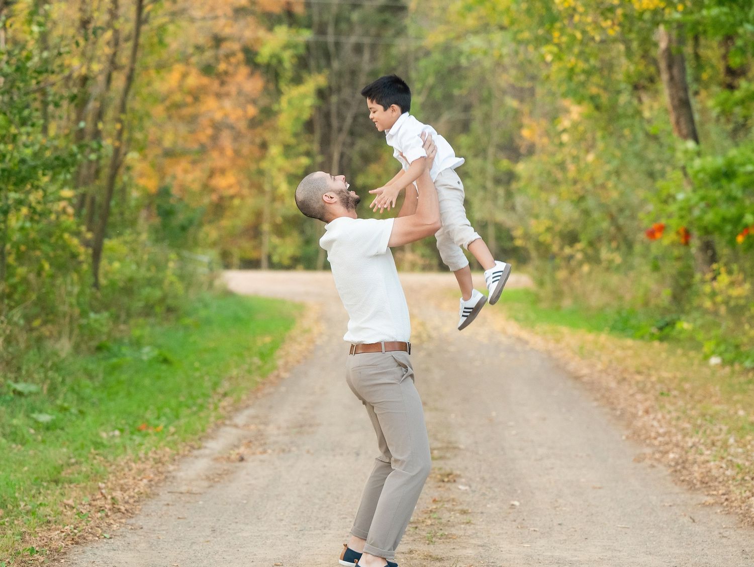 A couple dances together on a dirt path surrounded by autumn trees and falling leaves.