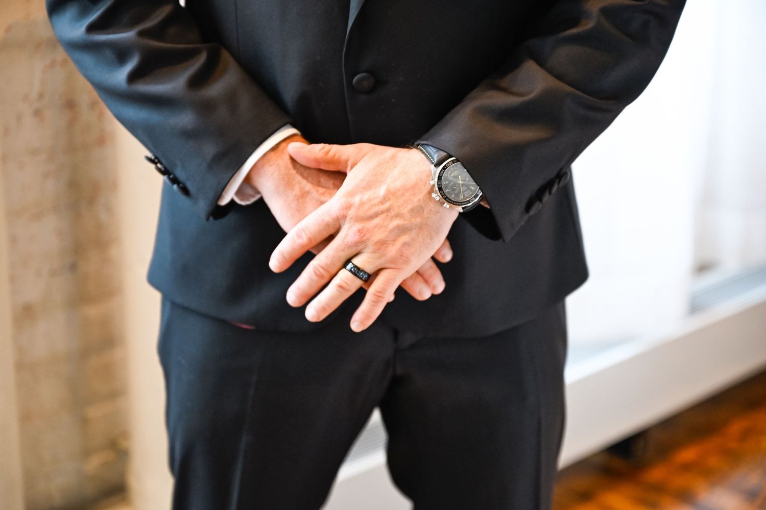 Groom in classic black tuxedo stands in elegant wedding venue setting.