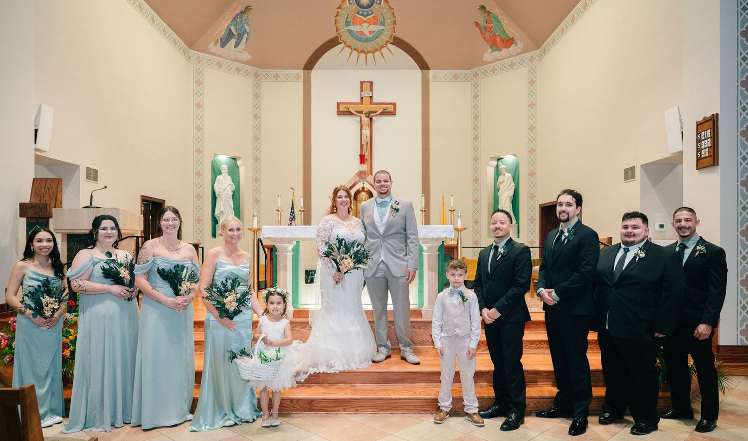 Wedding party poses at church altar with bridesmaids in mint gowns and groomsmen in black suits.