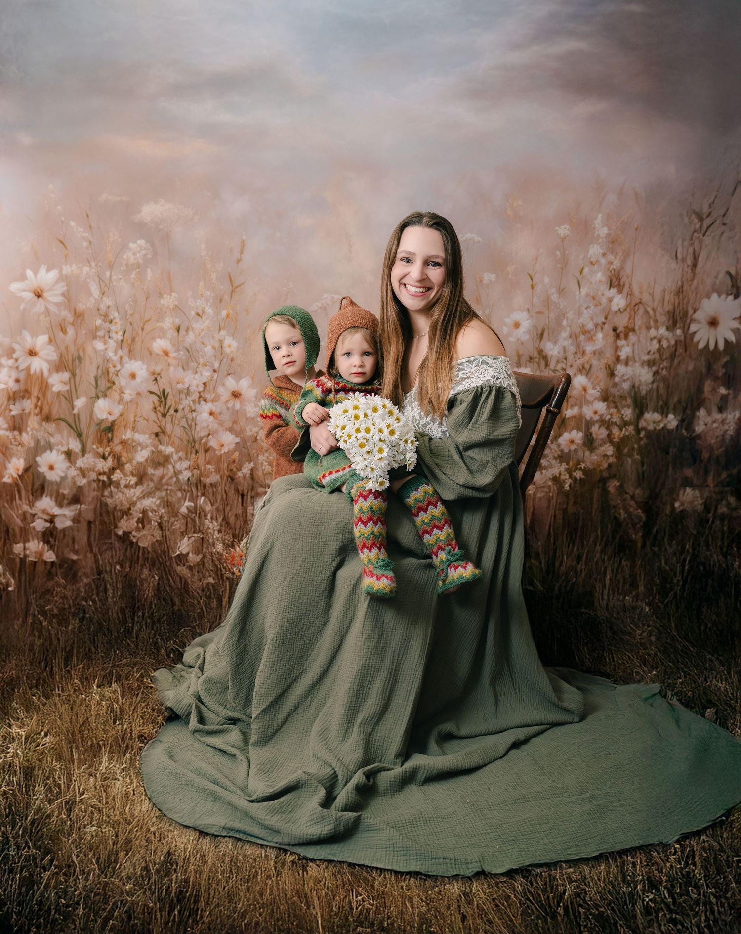 Woman in green dress holds child in colorful knit outfit with flowers, posed before floral field backdrop. mother day photoshoot