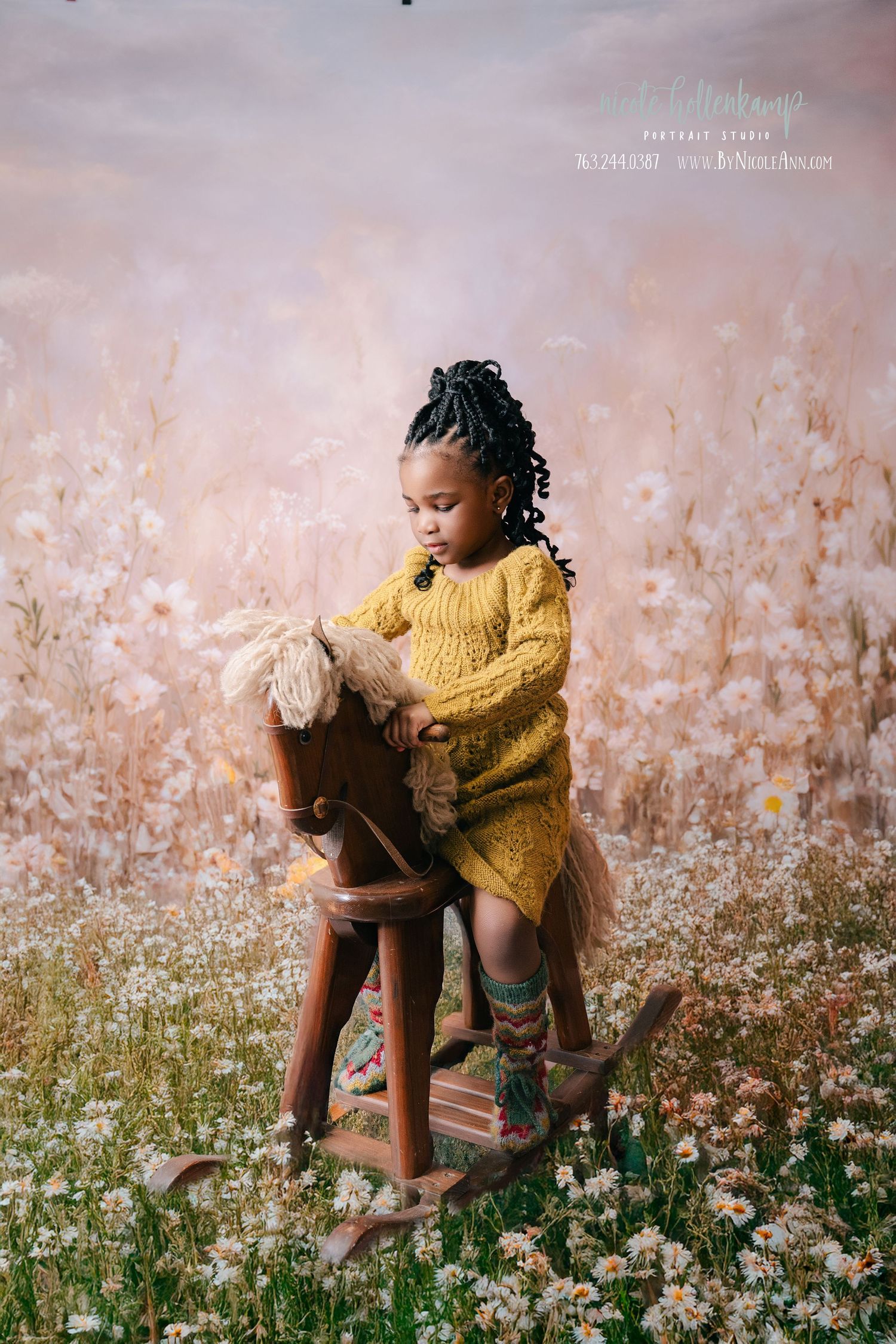 A young Black girl in a yellow knit dress sits on a wooden rocking horse surrounded by wildflowers in a dreamy floral setting. mother day ph