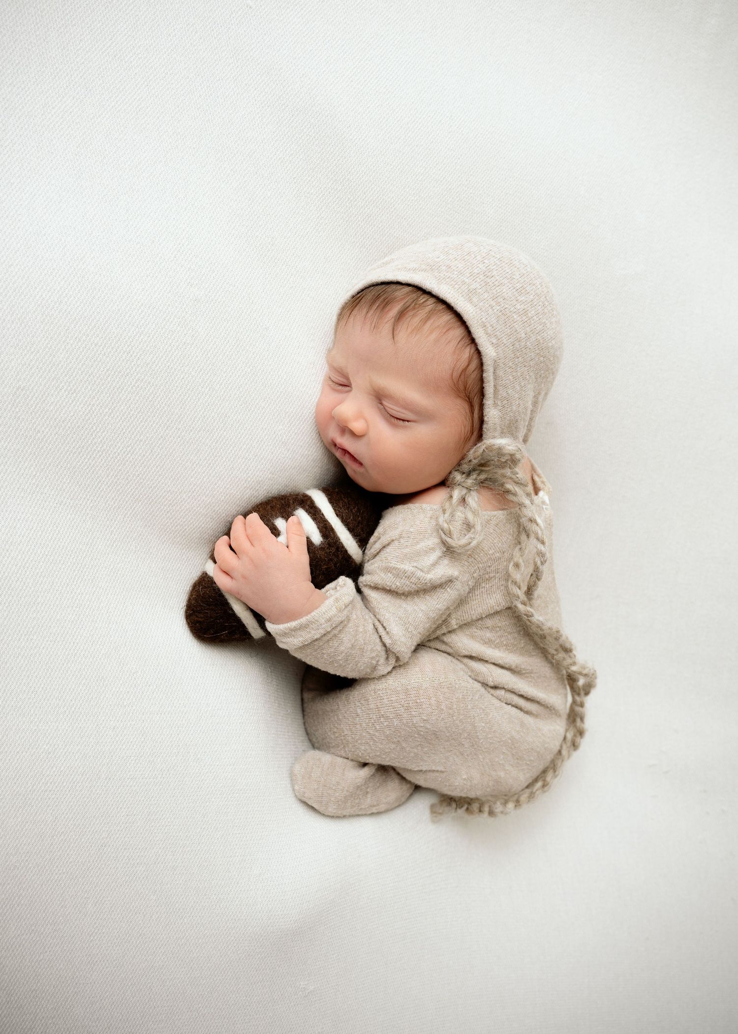 Minnesota Best newborn photographer - Peaceful sleeping newborn in cream-colored bonnet and onesie curled up on soft white backdrop.