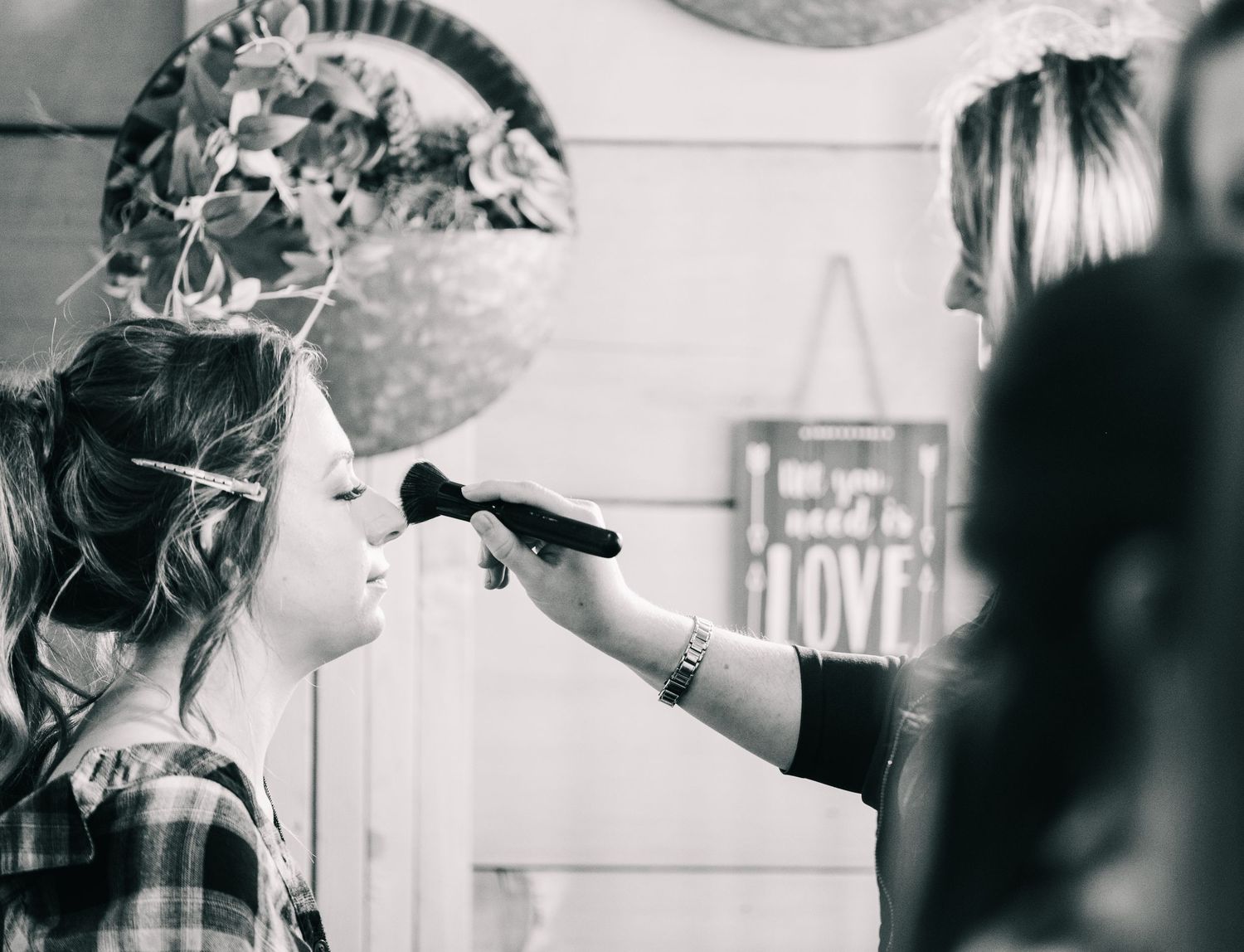 Black and white photo of makeup artist applying powder to bride during wedding day preparations.