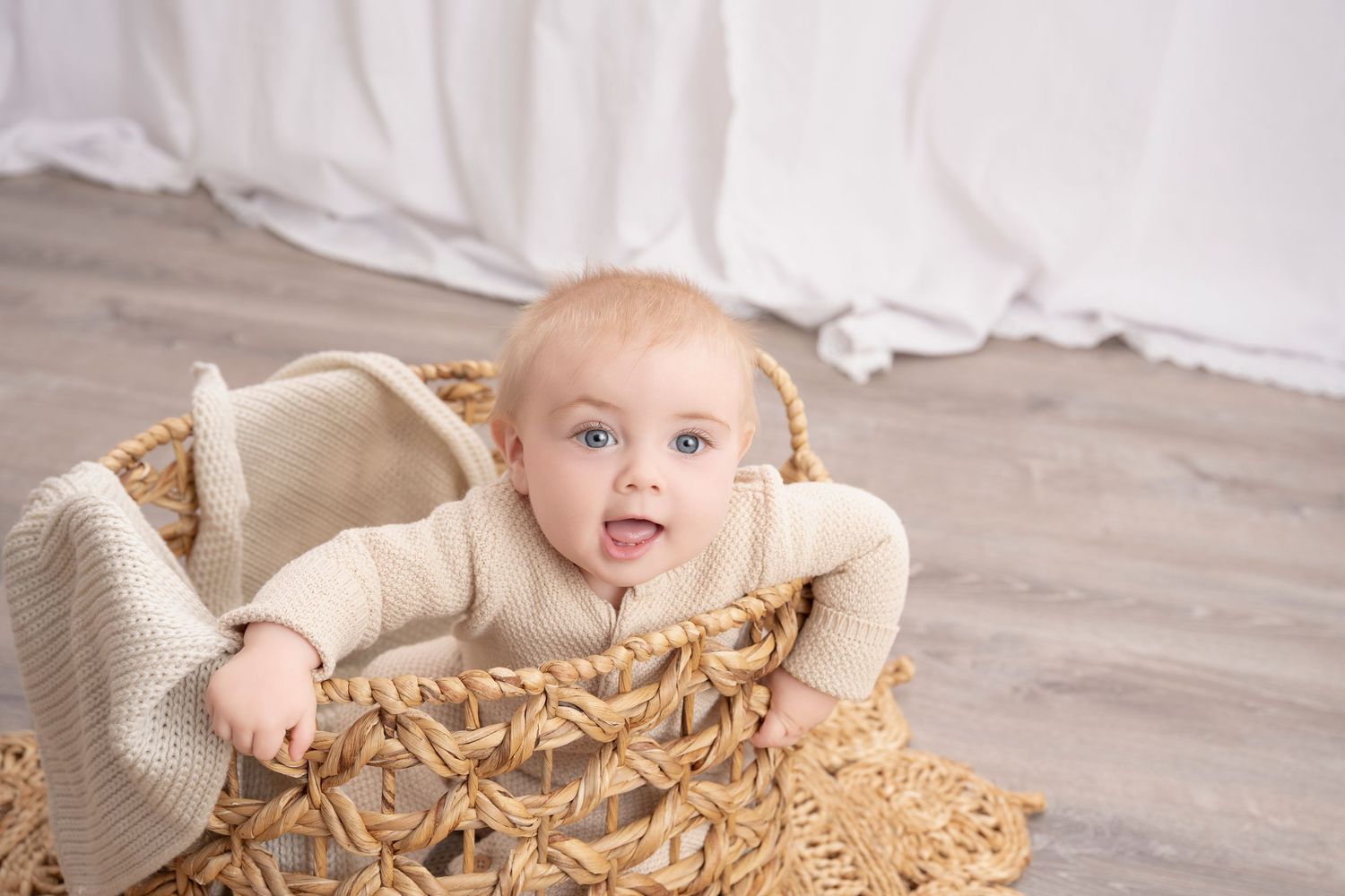 Central MN Milestone Photography - blue-eyed baby sitting in a woven wicker basket with a cream knit blanket in a bright white studio.