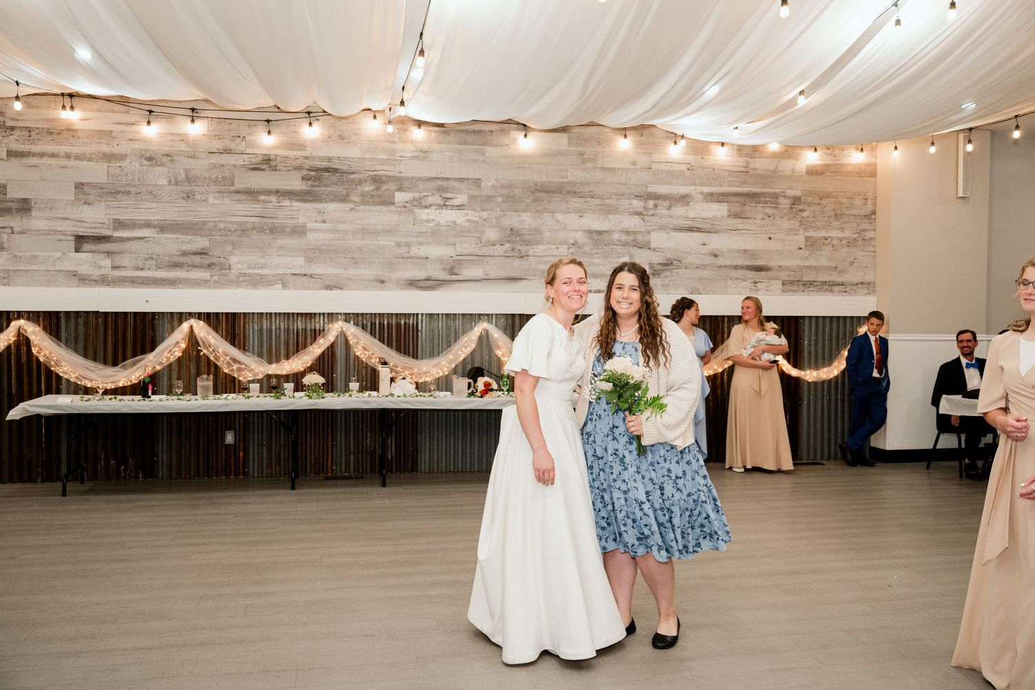 Dance floor at wedding reception with string lights and white fabric draping overhead in rustic venue.
