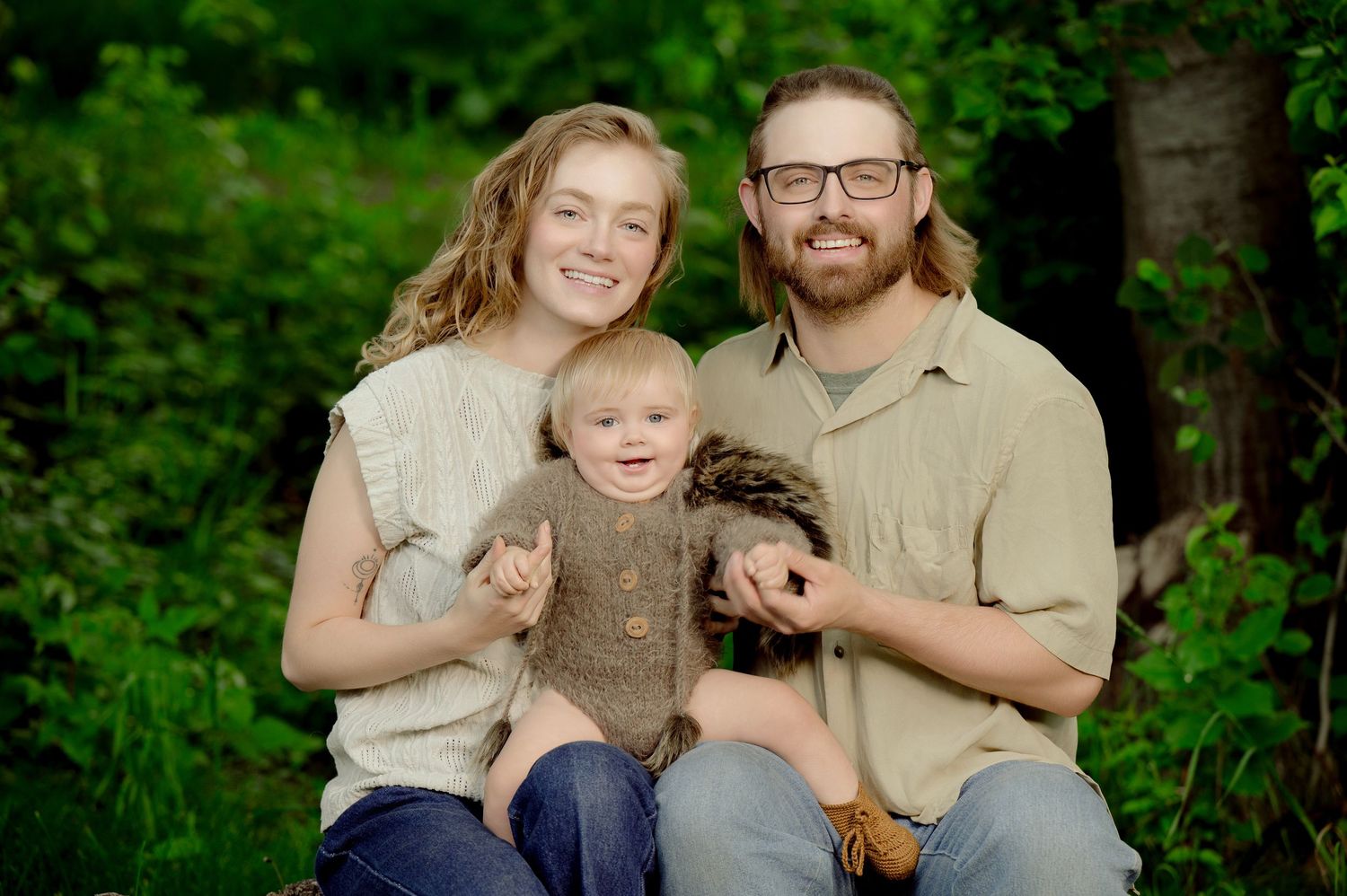 A family sits together outdoors for a portrait against a green forest background.
