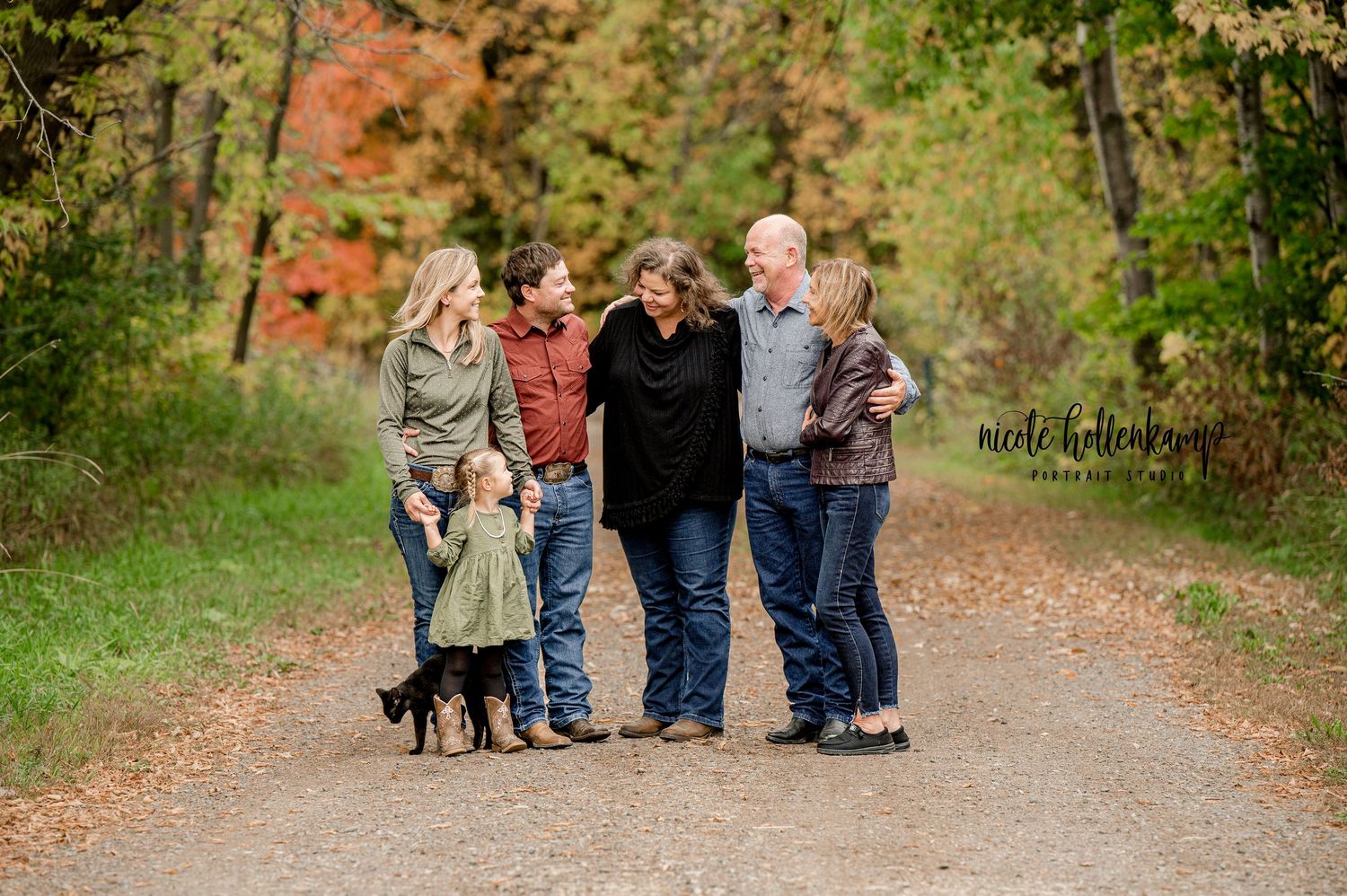 Multi-generational family enjoys a walk with their dog on a tree-lined autumn path.