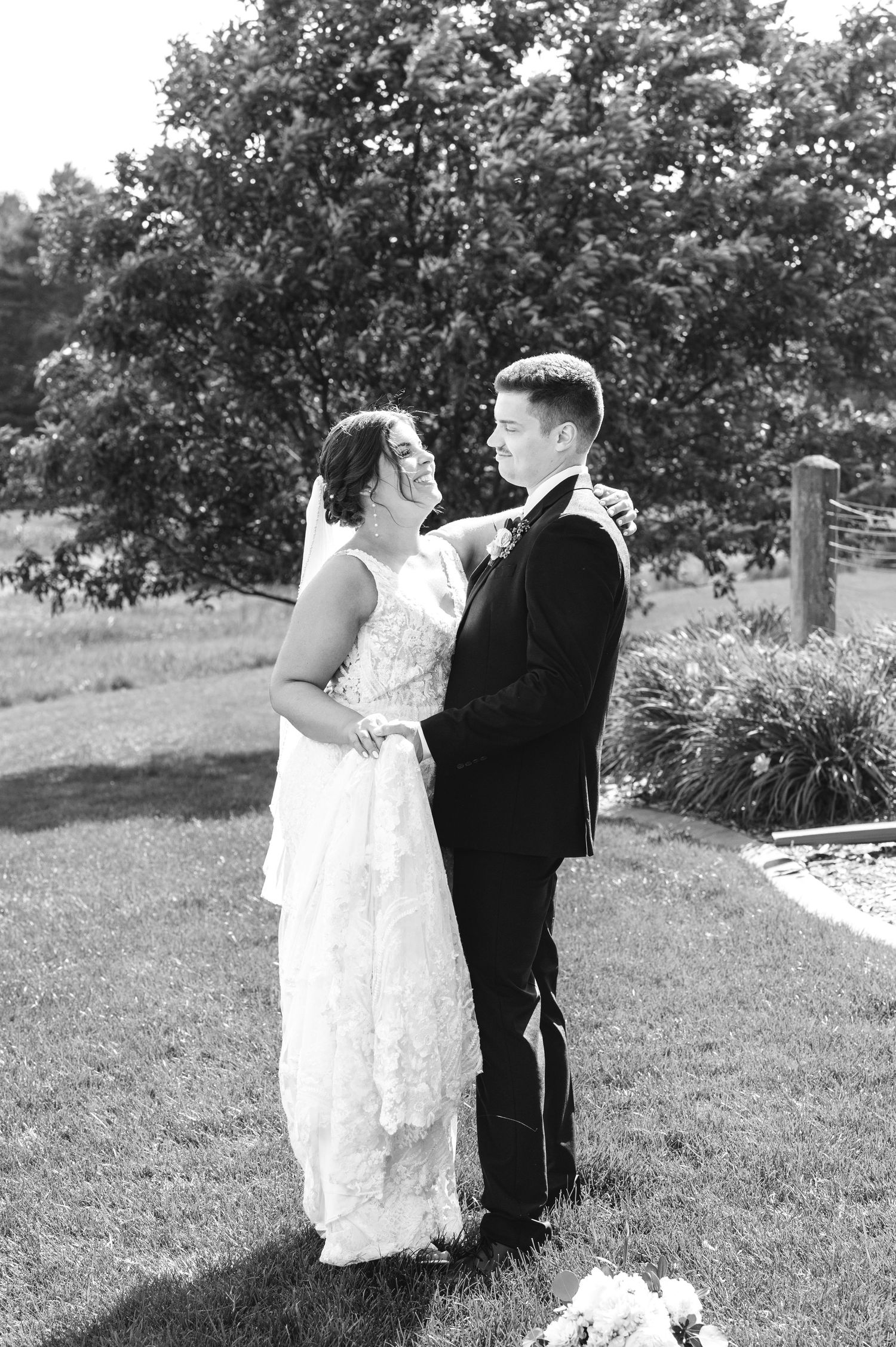 Black and white photo of bride and groom sharing a tender moment on green lawn outdoors.