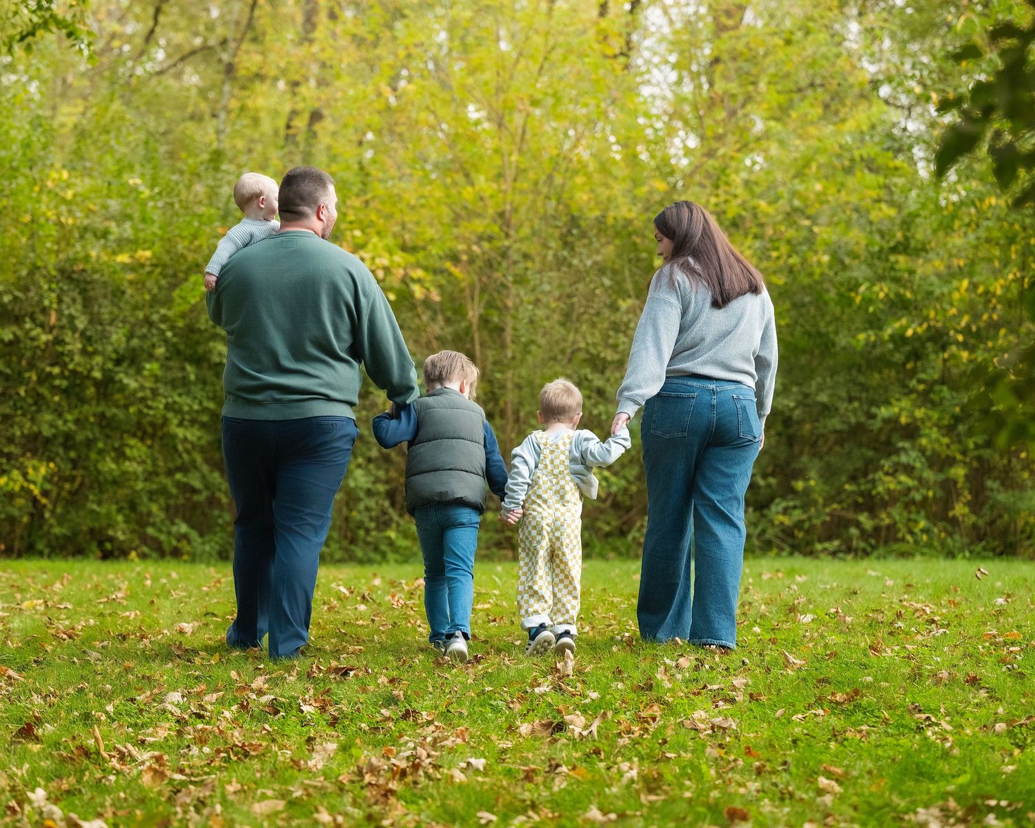 Family group walking together on grass with autumn trees in the background.
