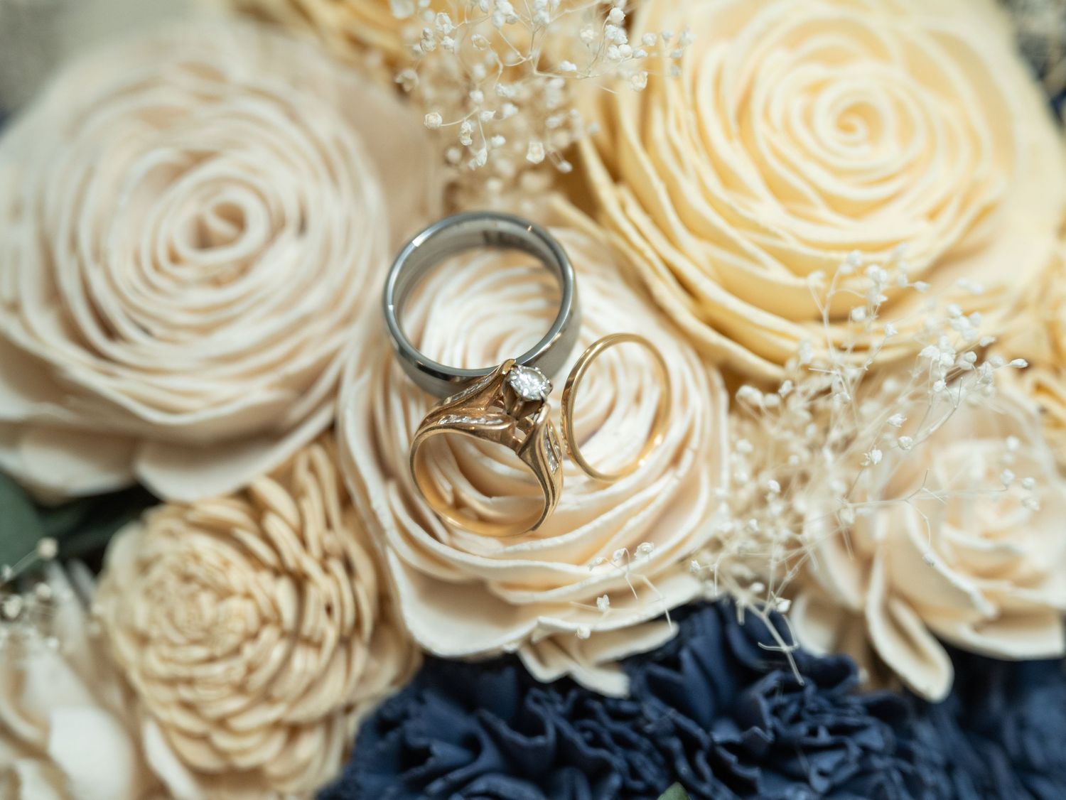 Wedding rings rest delicately on cream-colored roses with navy blue floral accents in an elegant arrangement.