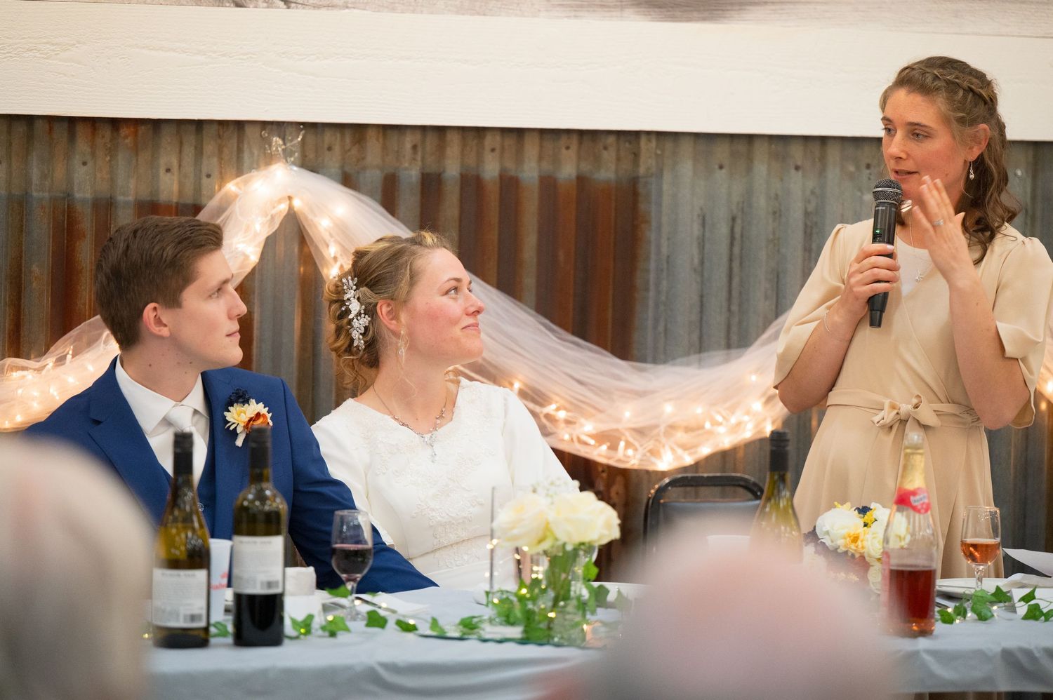 Wedding reception guests seated at long tables decorated with greenery and white floral centerpieces.