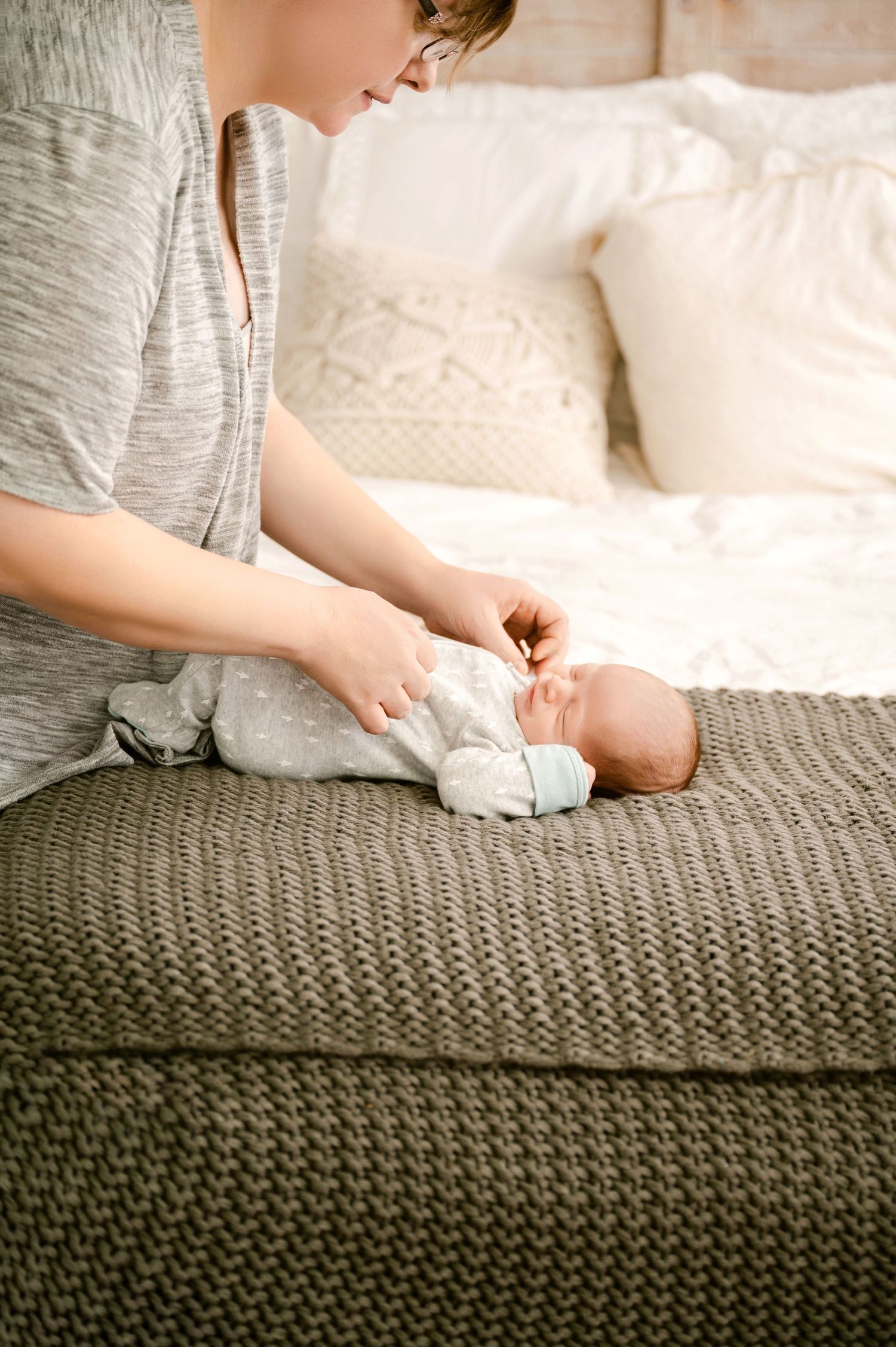 Gentle moment during diaper change on textured grey knit blanket with white pillows in background.