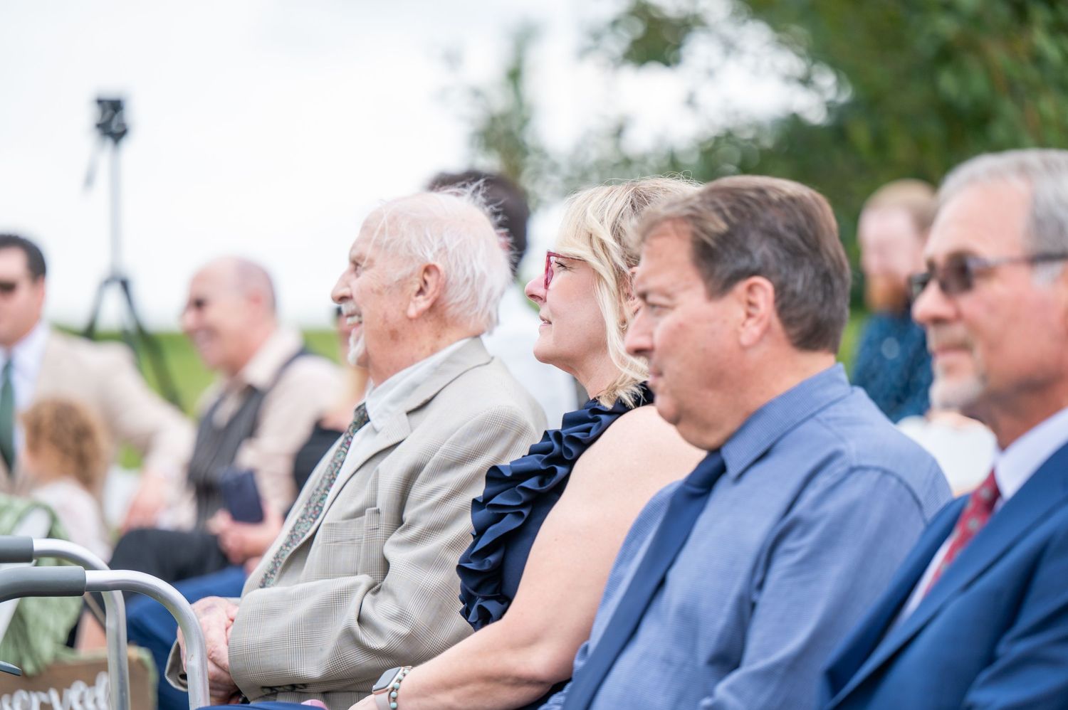Wedding guests seated in chairs watch outdoor ceremony unfold.