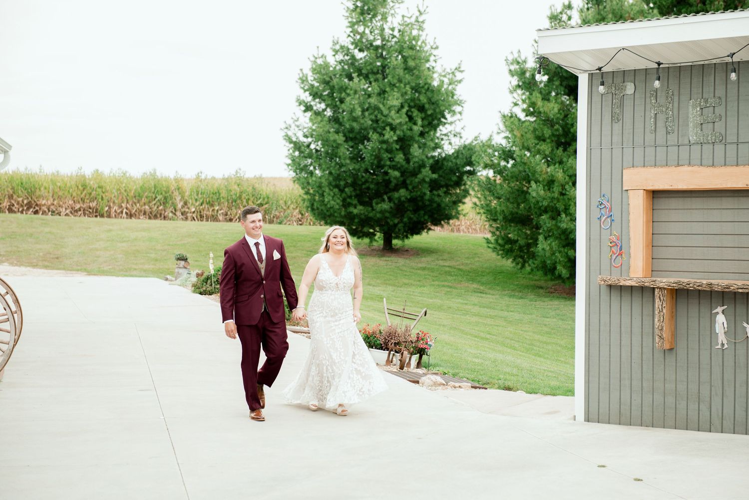 Wedding couple walks along a paved path with their dog beside a rustic building on their special day.