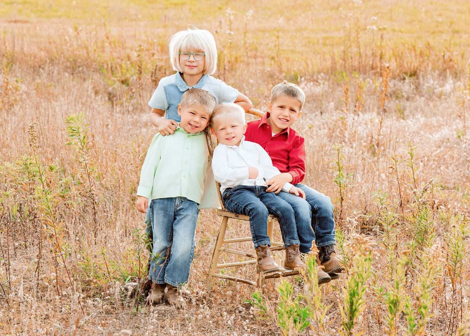 Three children pose together on a wooden chair in a golden autumn field.