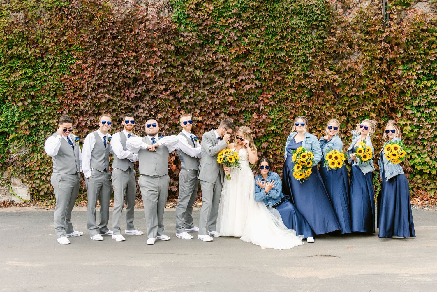 Central MN Wedding Photos | Wedding party in gray suits and blue dresses with sunflowers posing against ivy wall.